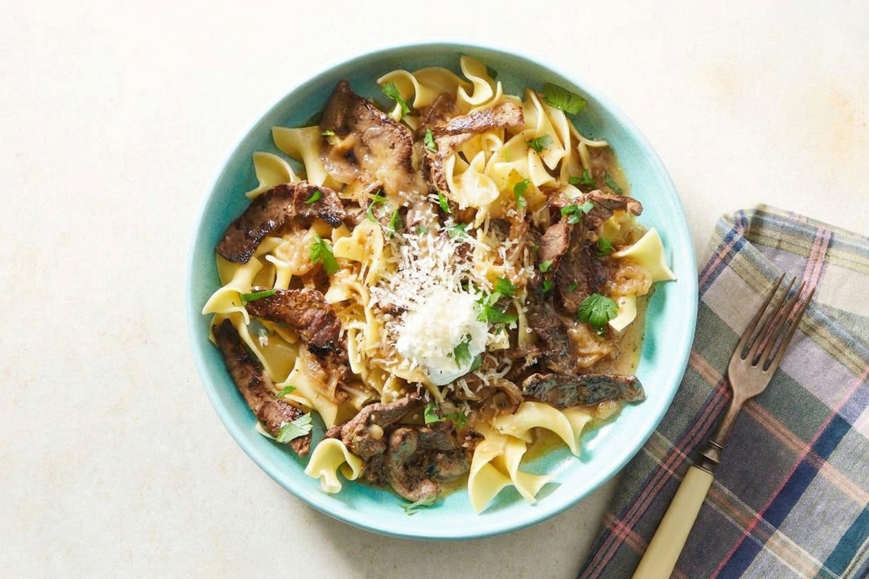 A plated serving of steak pasta topped with chopped parsley and extra Parmesan on a simple dinner table setting