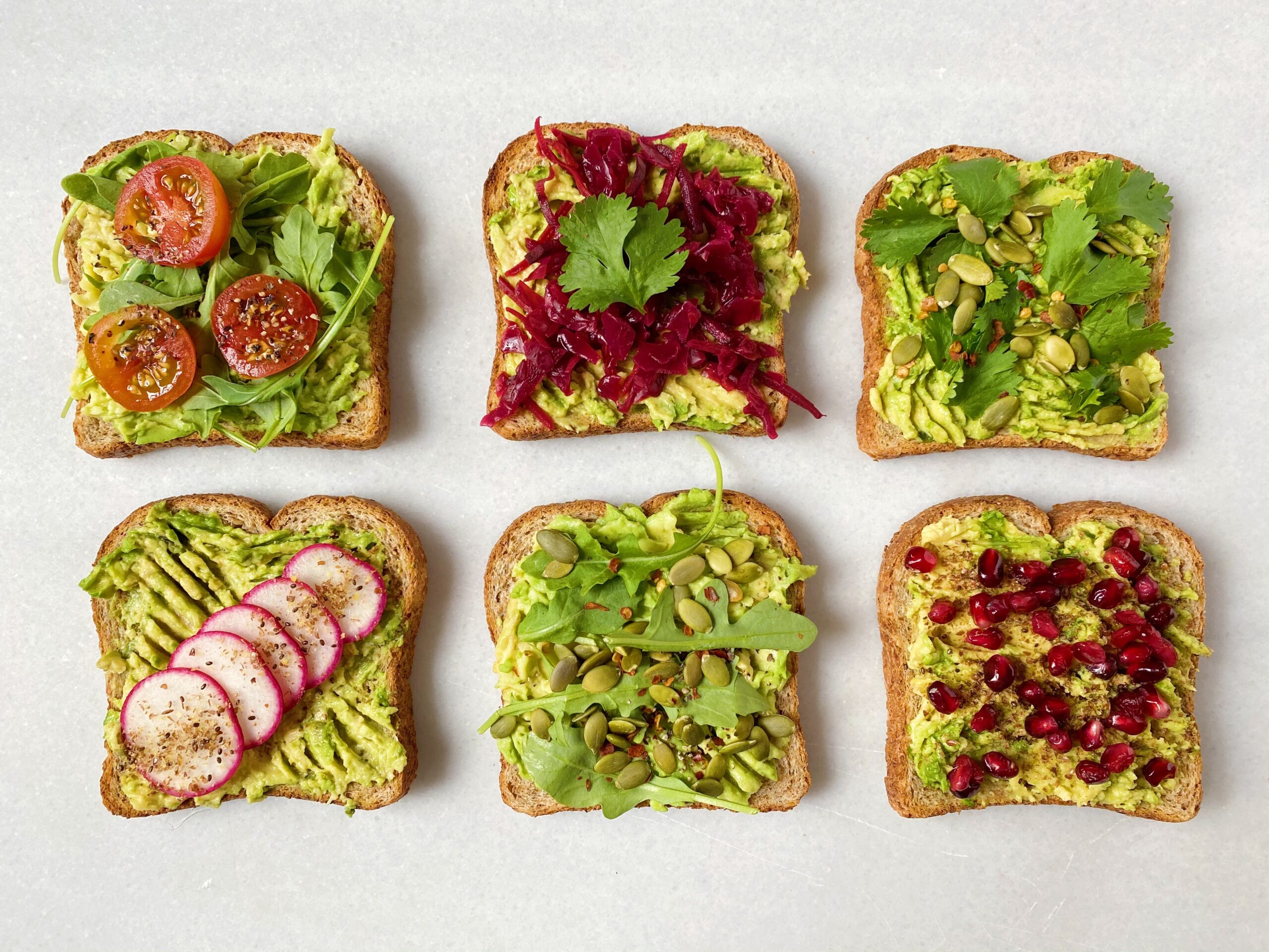 A plated slice of Ezekiel bread avocado toast topped with chili flakes and flaky salt on a neutral ceramic plate on a sunlit kitchen table