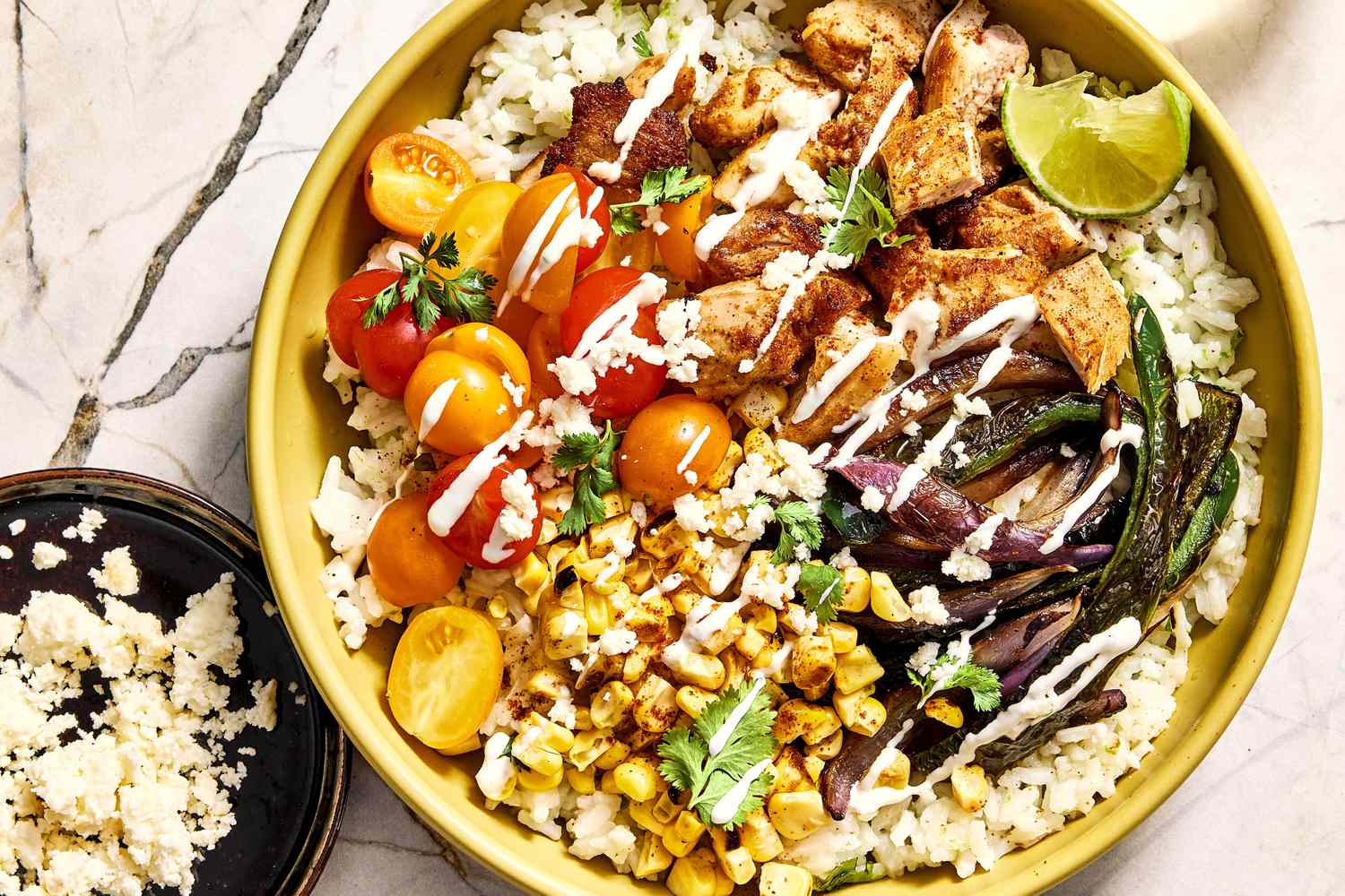 A plated street corn chicken rice bowl with charred corn, sliced spiced chicken, crumbled cotija, cilantro, and lime wedges on a wooden table with soft natural light