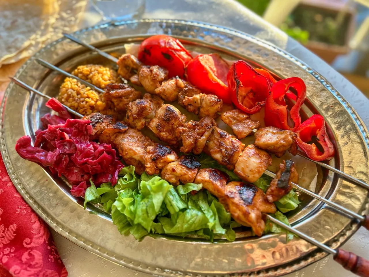 A platter of Turkish chicken shish kebabs with charred edges, served with lemon wedges, sliced red onion, parsley, and warm flatbread on a wooden table