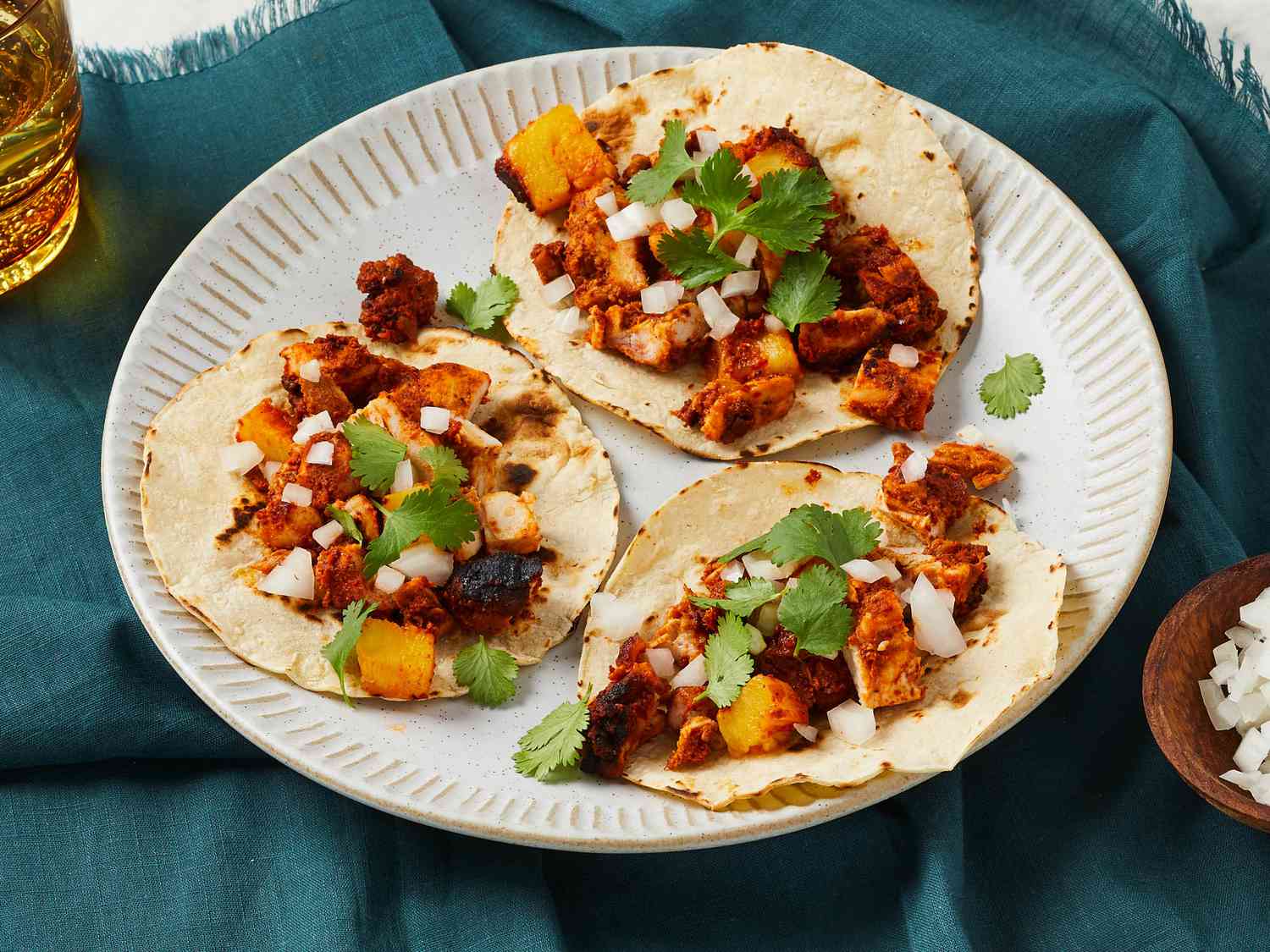 A platter of chicken al pastor with charred pineapple, chopped onion, cilantro, and lime wedges set on a warm kitchen table