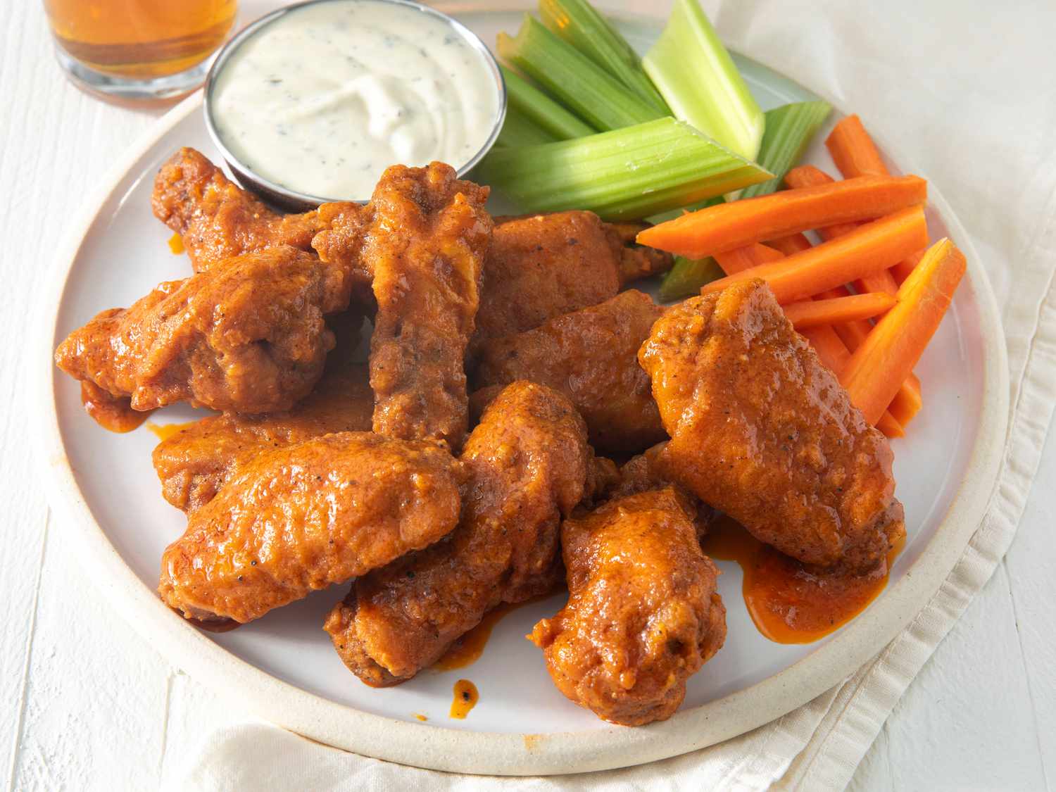 A platter of crispy Buffalo chicken wings glossy with orange-red sauce, served with celery sticks and a small bowl of blue cheese dressing on a wooden table