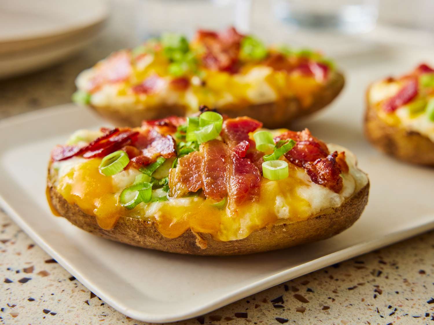 A platter of double stuffed baked potatoes with golden browned tops, melted cheddar, crispy bacon bits, and chopped chives on a warm kitchen table