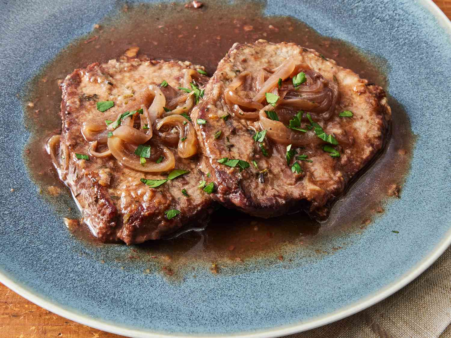 A platter of fork-tender braised eye of round steak sliced and spooned with glossy onion gravy, served with mashed potatoes on a rustic dinner table