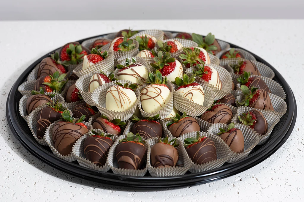 A platter of glossy chocolate covered strawberries with a few drizzled in white chocolate on a light kitchen counter in warm natural light