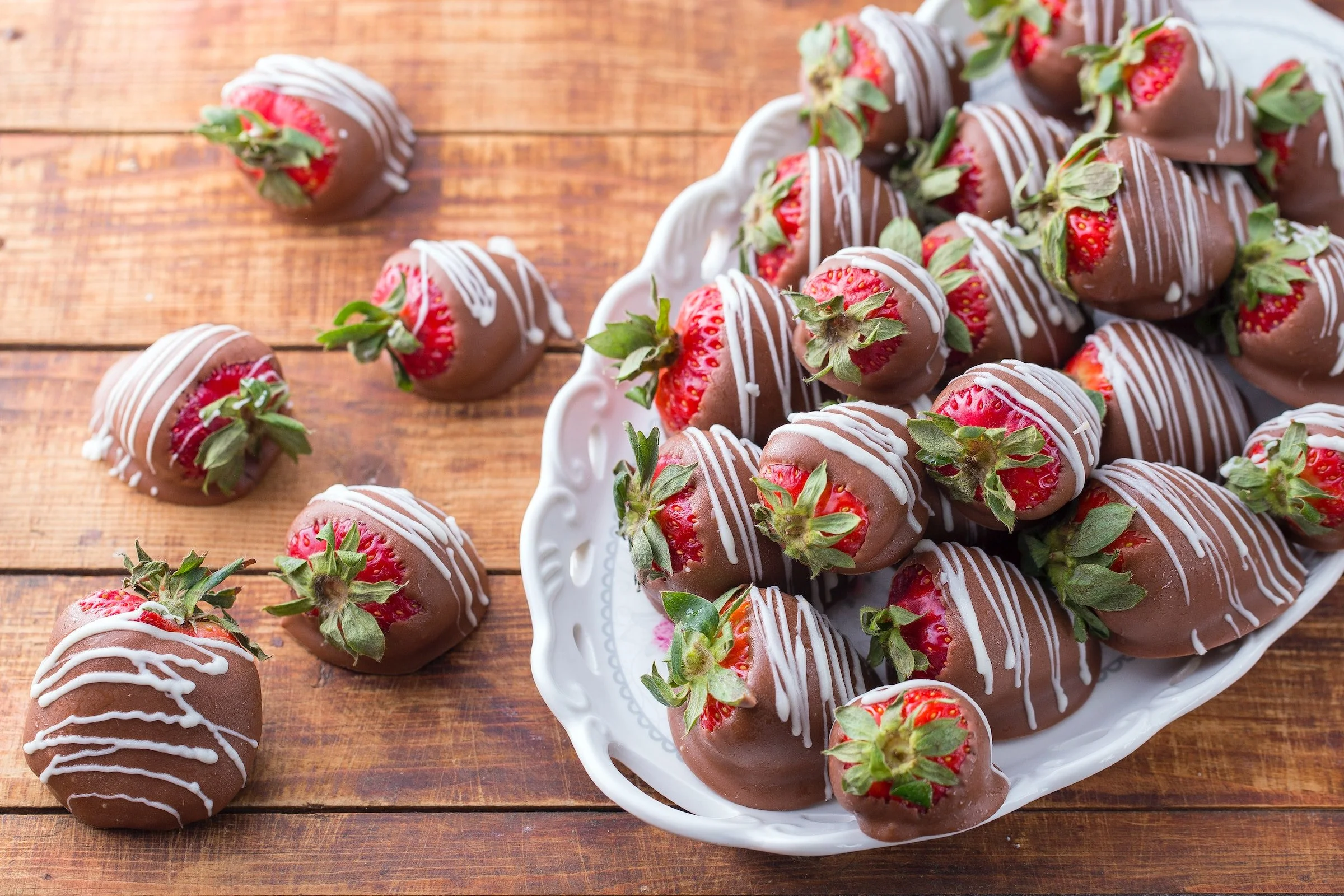 A platter of glossy chocolate covered strawberries with a few drizzled in white chocolate on a neutral linen table setting