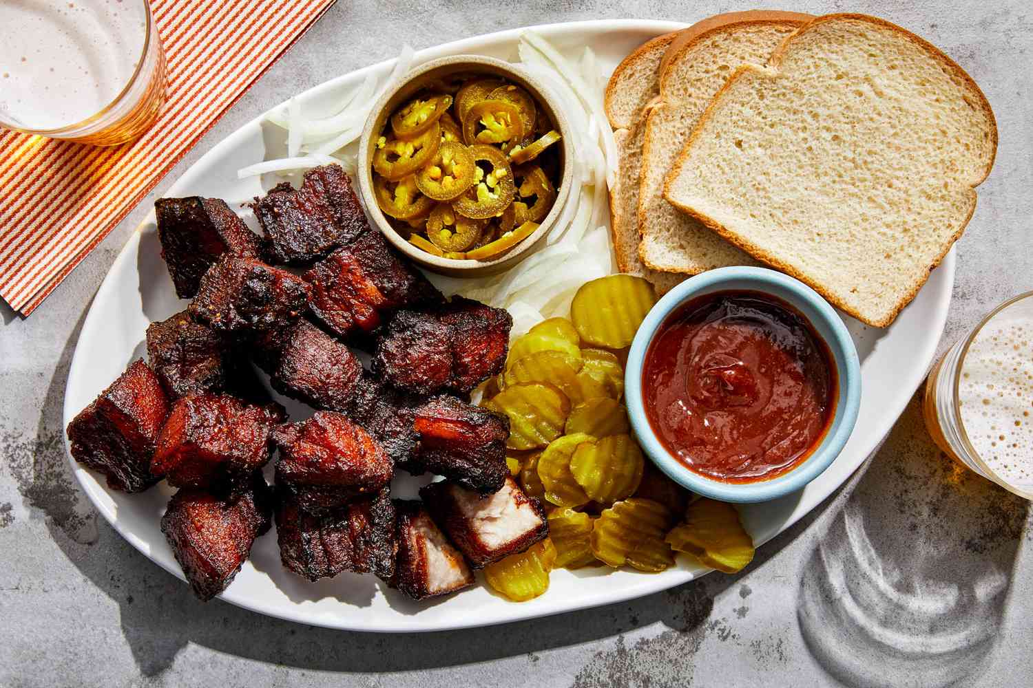 A platter of glossy pork belly burnt ends with caramelized edges, sprinkled with sliced scallions, set on a warm wooden table with a small bowl of extra barbecue sauce