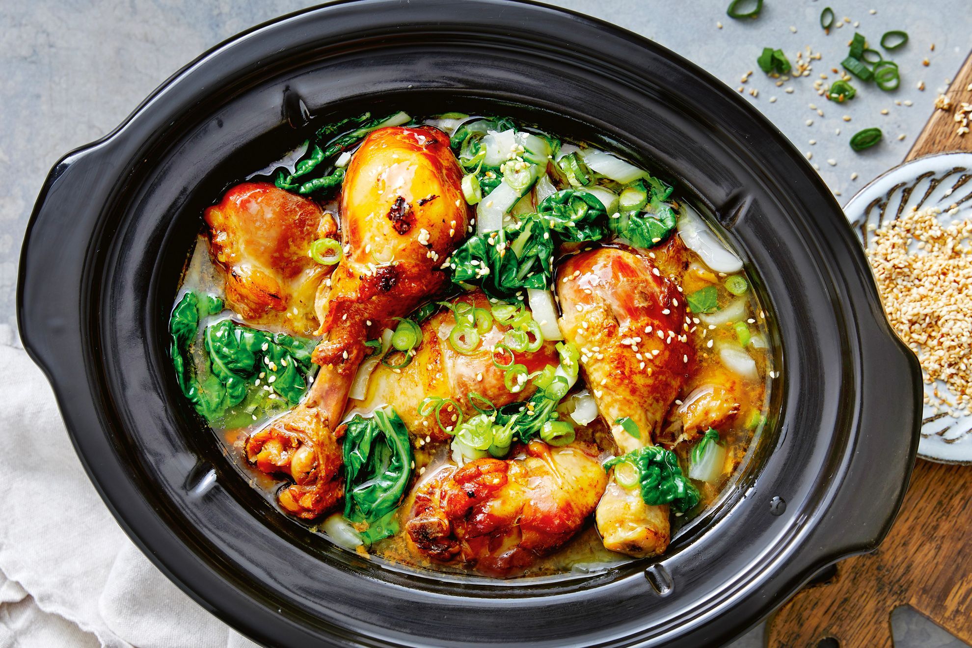 A platter of glossy slow cooker chicken drummies with caramelized edges, sprinkled with sliced green onions on a wooden table setting