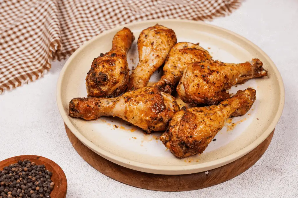 A platter of golden brown air fryer chicken drumsticks with crispy skin, garnished with lemon wedges and chopped parsley on a wooden dinner table with simple plates