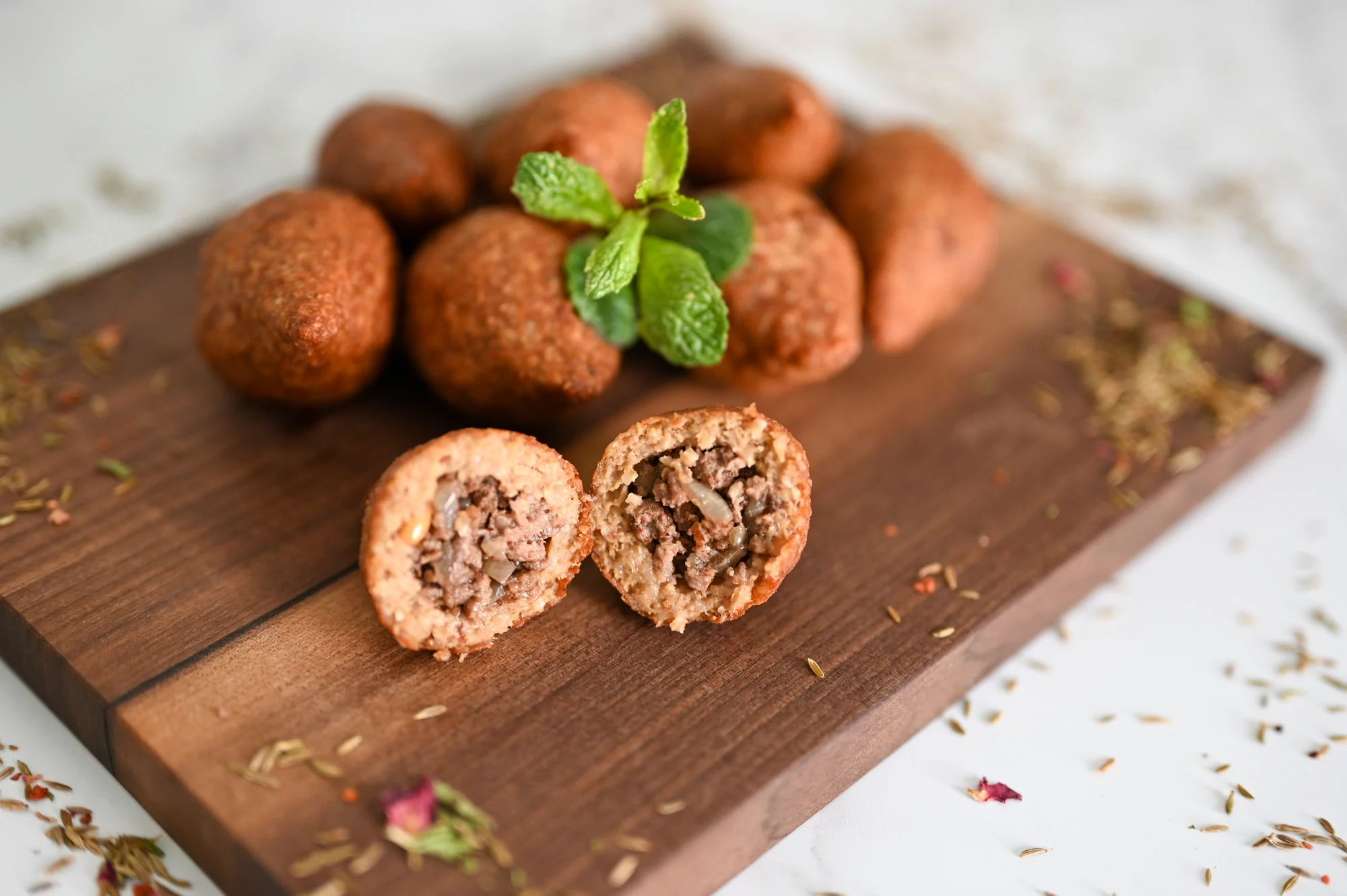 A platter of golden brown fried kibbeh arranged on a white serving plate with lemon wedges and a small bowl of yogurt sauce on a wooden table
