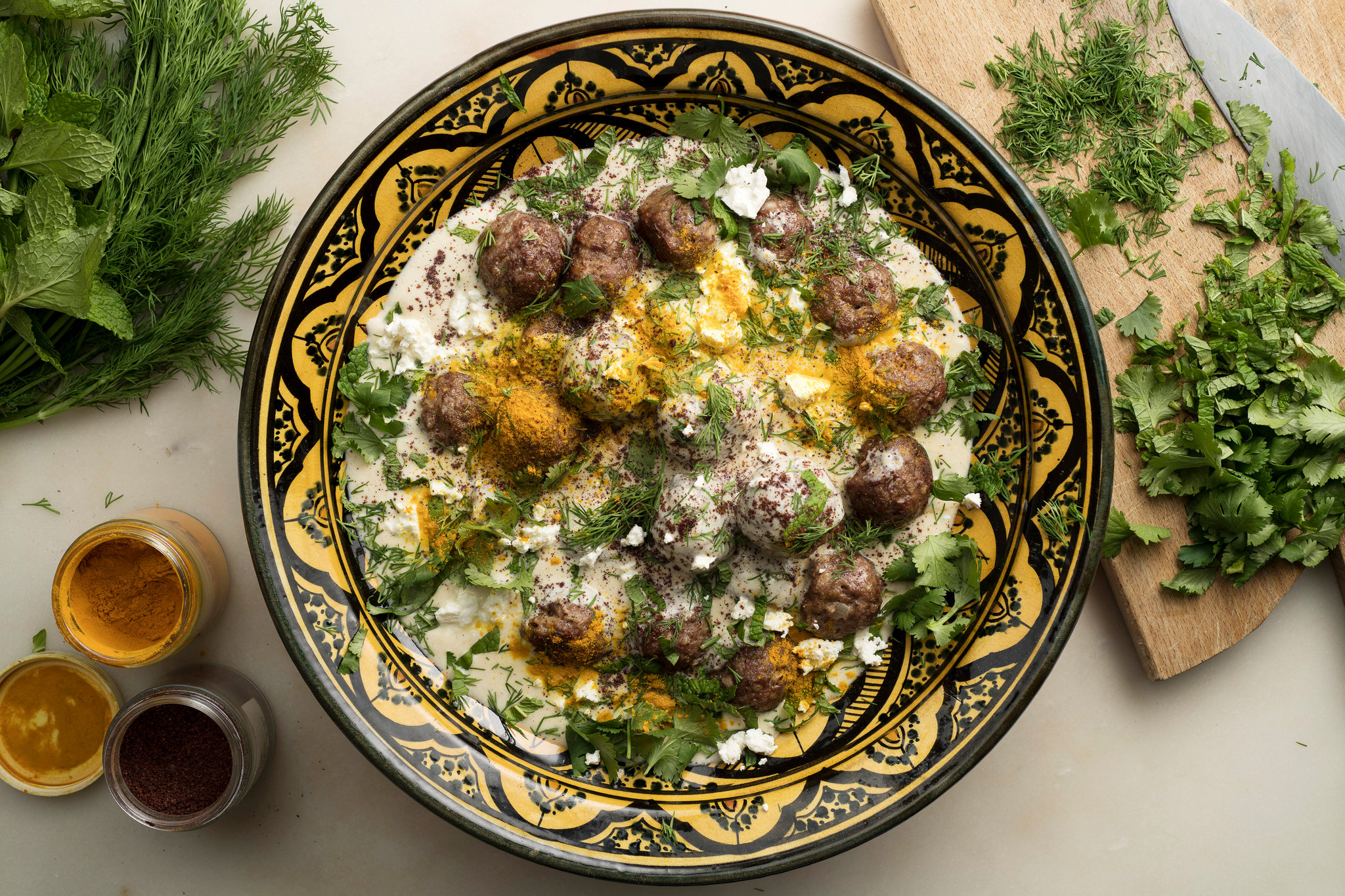 A platter of golden-brown lamb meatballs piled high with a bowl of lemon herb yogurt sauce on a wooden table setting