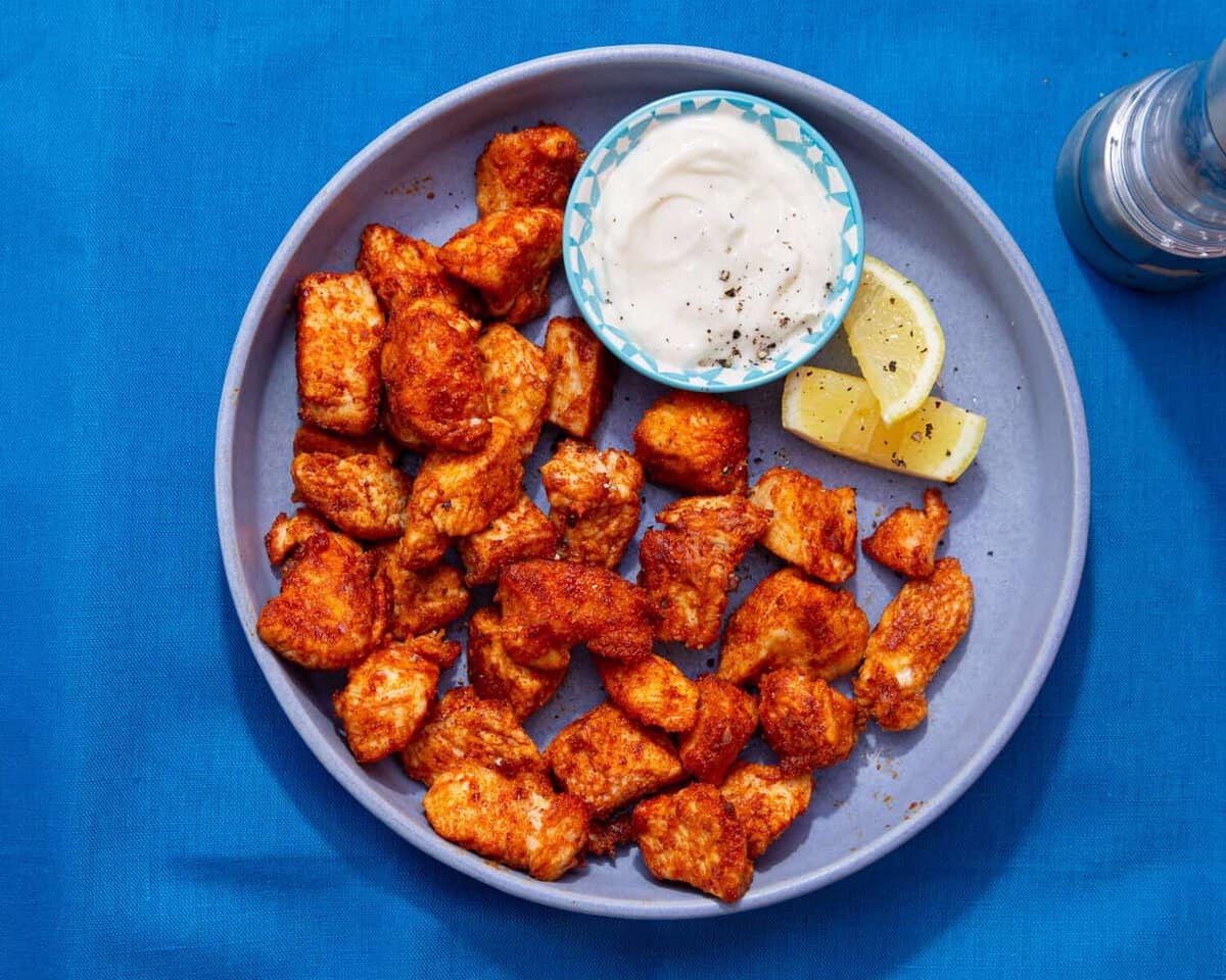 A platter of golden, crispy garlic Parmesan chicken bites with a small bowl of lemony yogurt dip on a cozy kitchen table