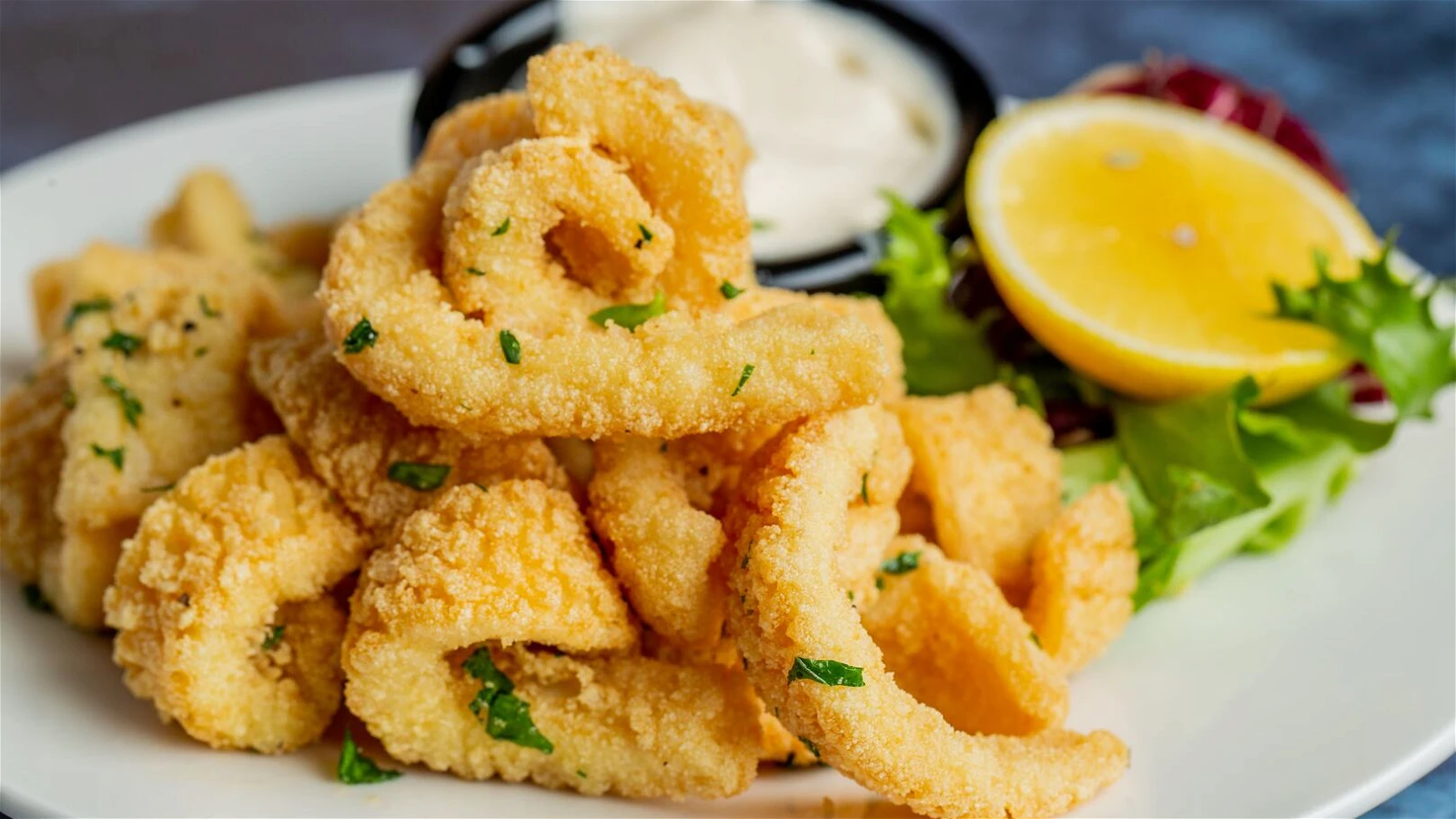 A platter of golden fried calamari rings and tentacles with lemon wedges and a small bowl of lemon garlic aioli on a wooden table