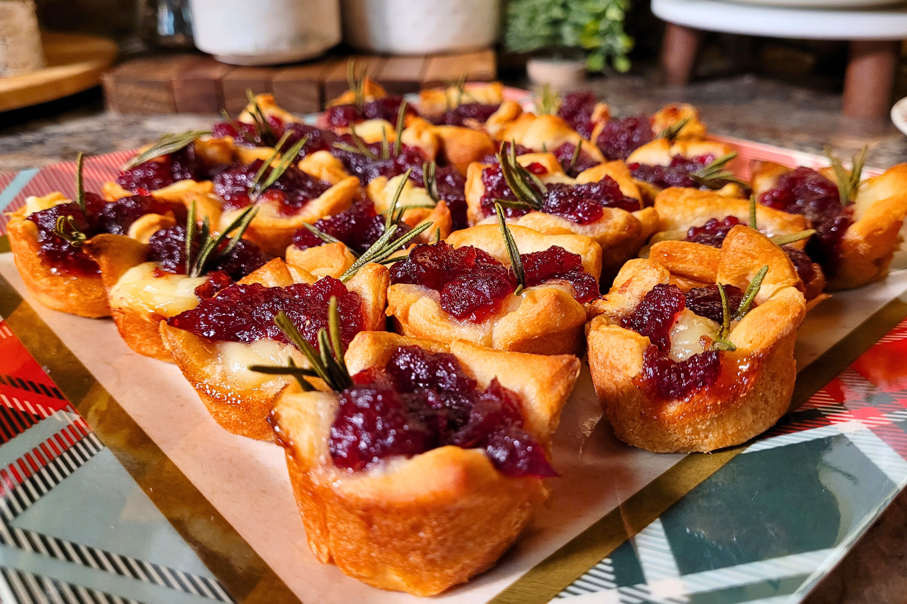 A platter of golden puff pastry cranberry brie bites with melty brie and glossy cranberry sauce, set on a cozy holiday table