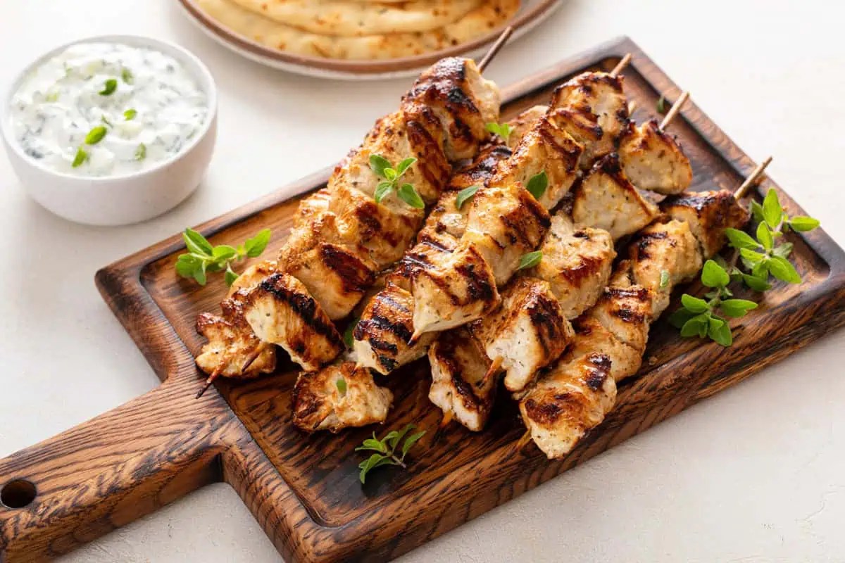 A platter of grilled chicken kebabs with charred edges, red onion and bell pepper pieces, and lemon wedges on a wooden table
