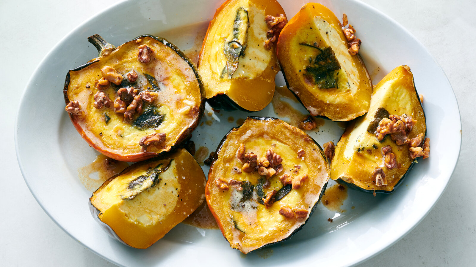 A platter of maple roasted custard squash halves with caramelized edges and a glossy butter glaze, set on a wooden table with a simple linen napkin