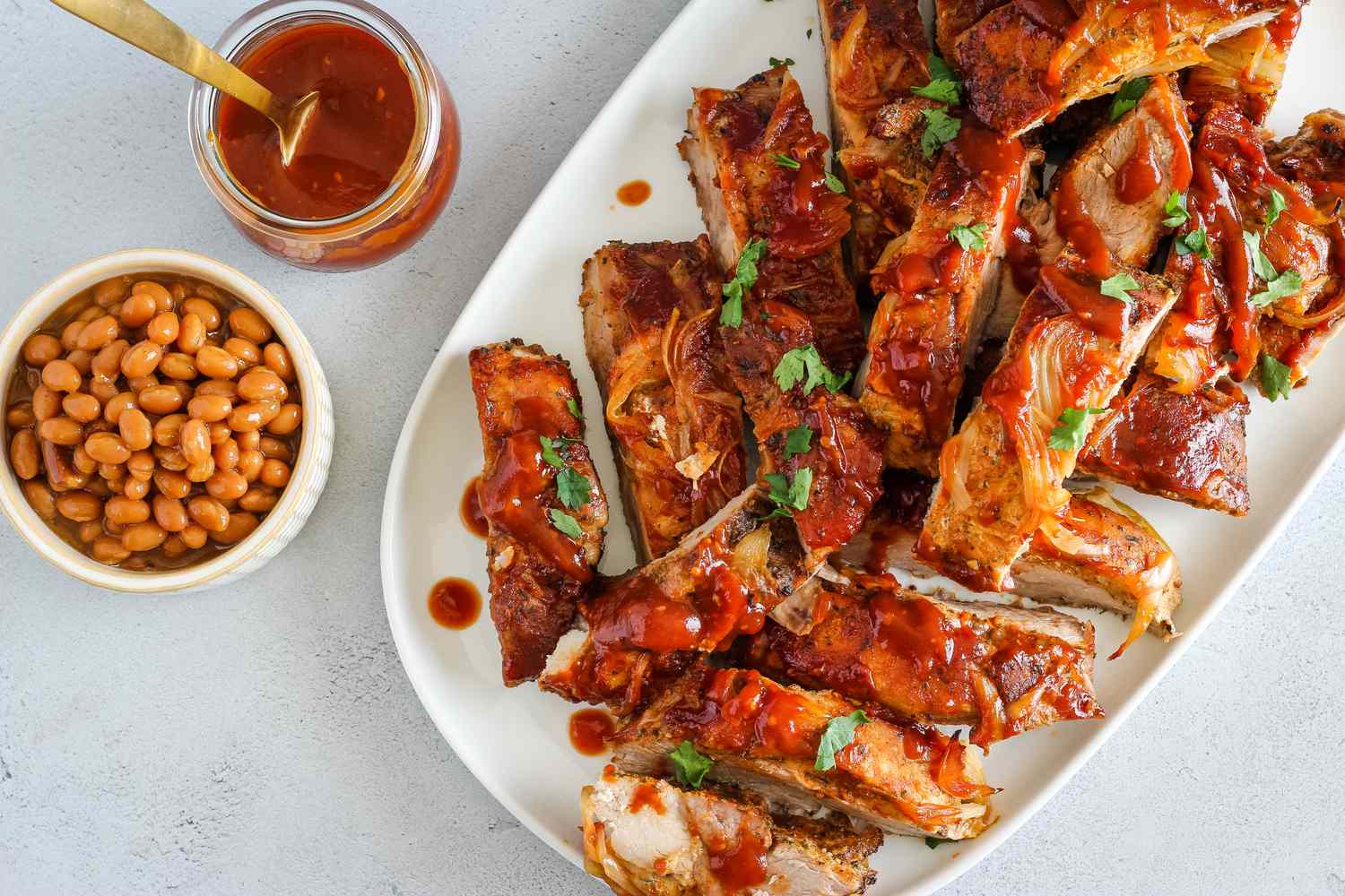 A platter of oven-baked country style ribs glazed with barbecue sauce, garnished with sliced green onions on a wooden table with warm kitchen lighting