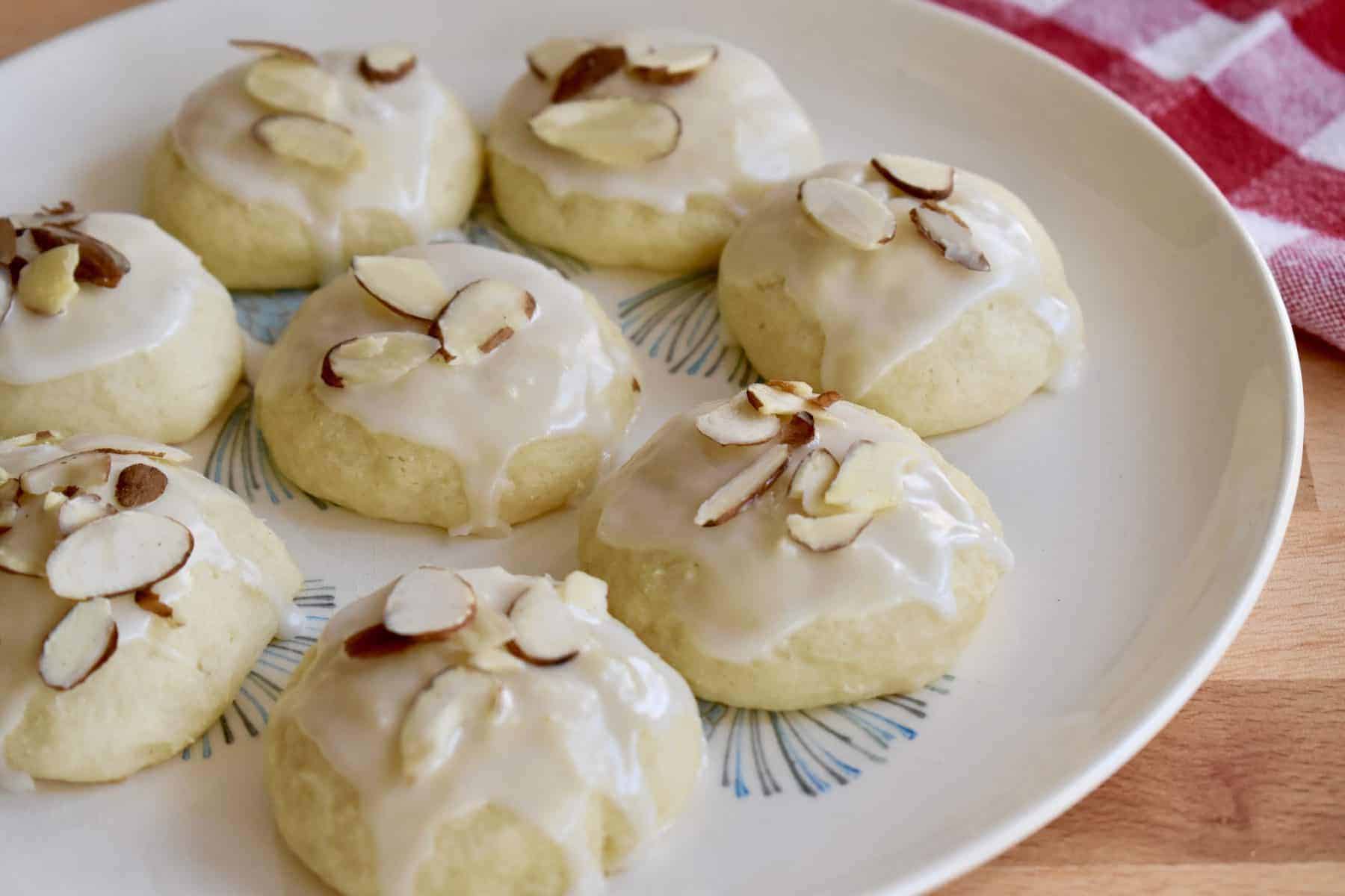 A platter of soft Italian ricotta cookies topped with glossy white glaze and colorful sprinkles on a warm kitchen table with afternoon light