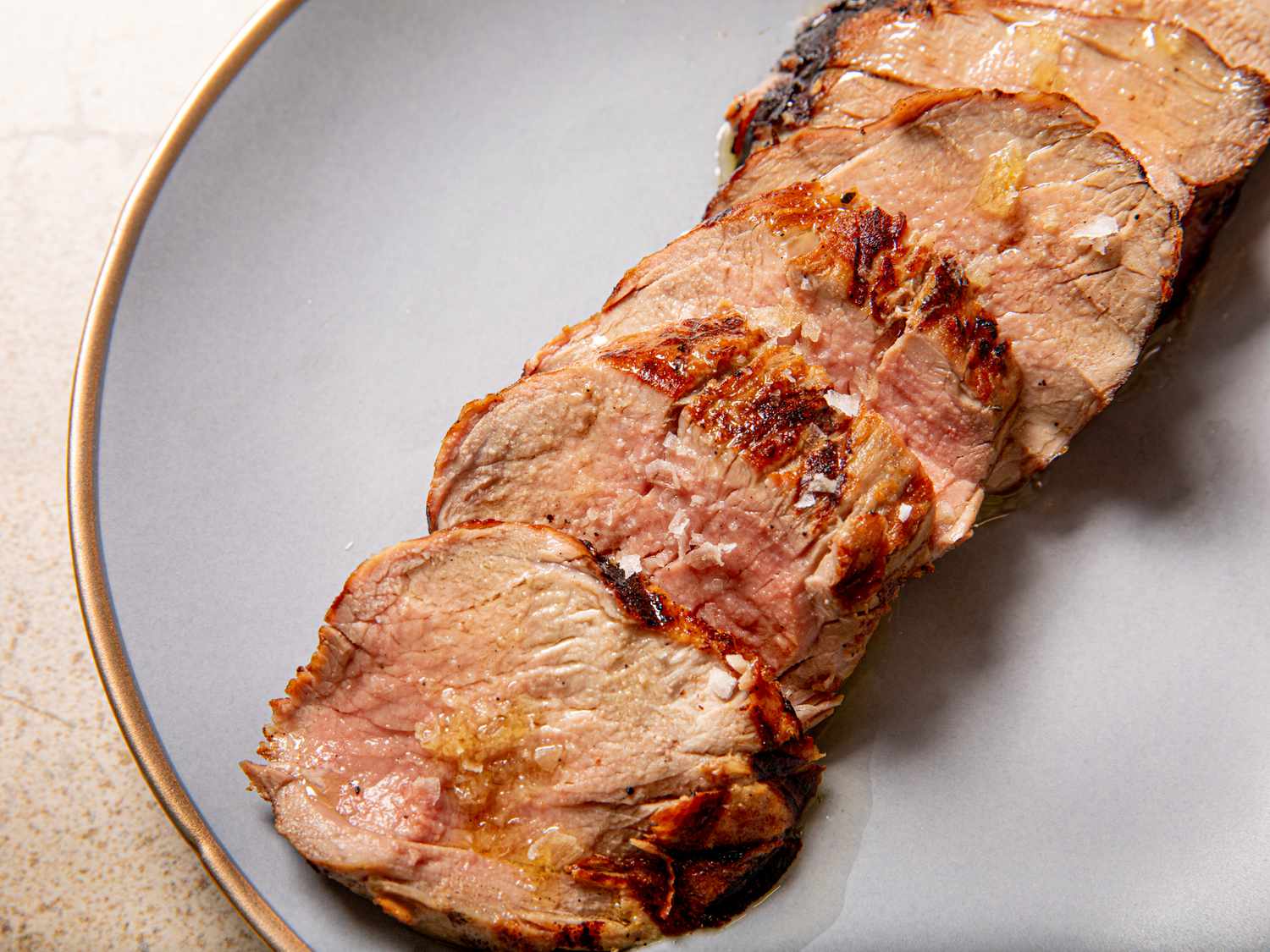 A pork fillet on a wooden cutting board being seasoned with salt, pepper, and paprika in a bright home kitchen