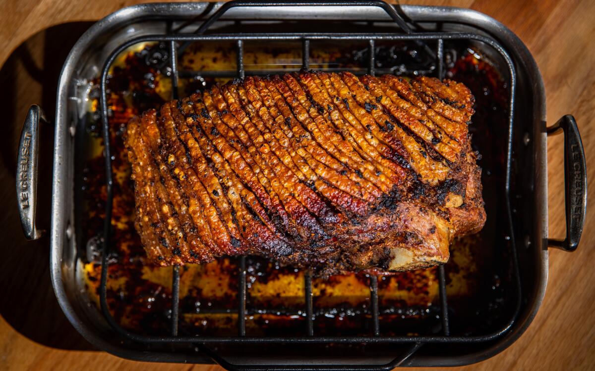 A pork shoulder roasting in a metal pan with citrus-garlic juices bubbling around it in a home oven