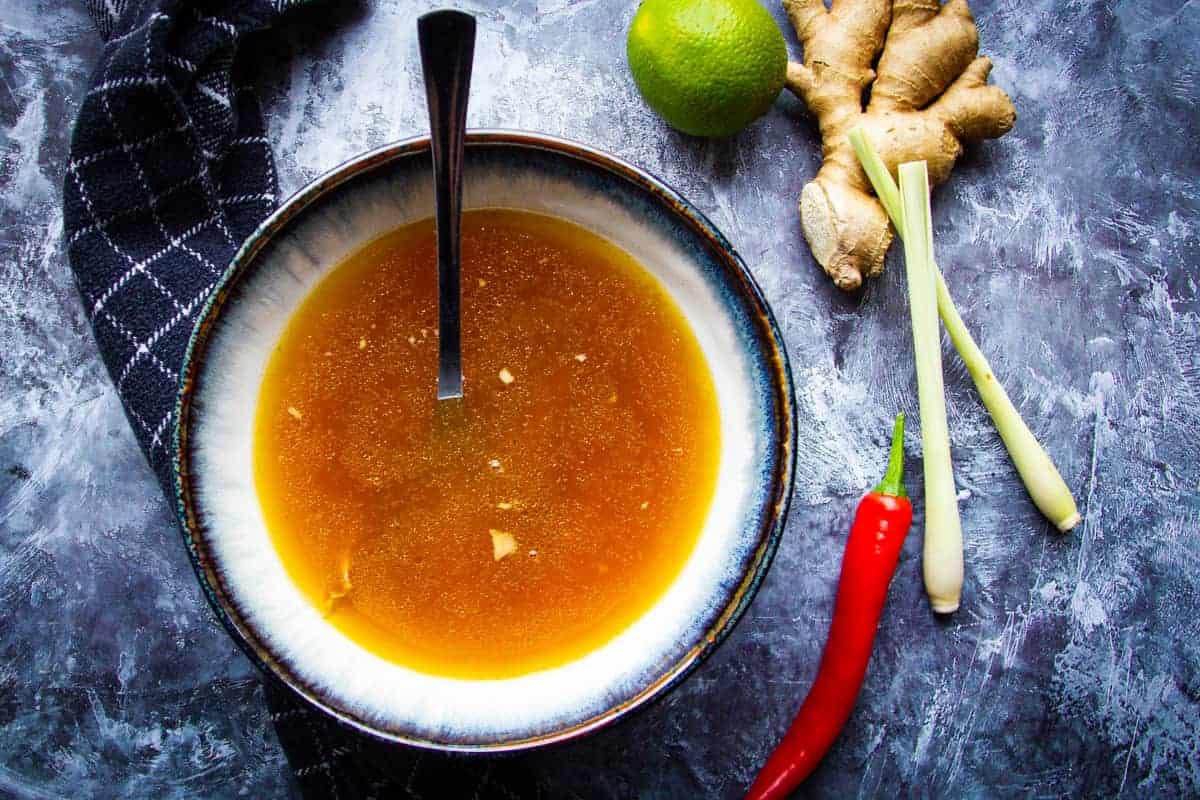 A pot of broth simmering with smashed lemongrass pieces and ginger slices floating on top
