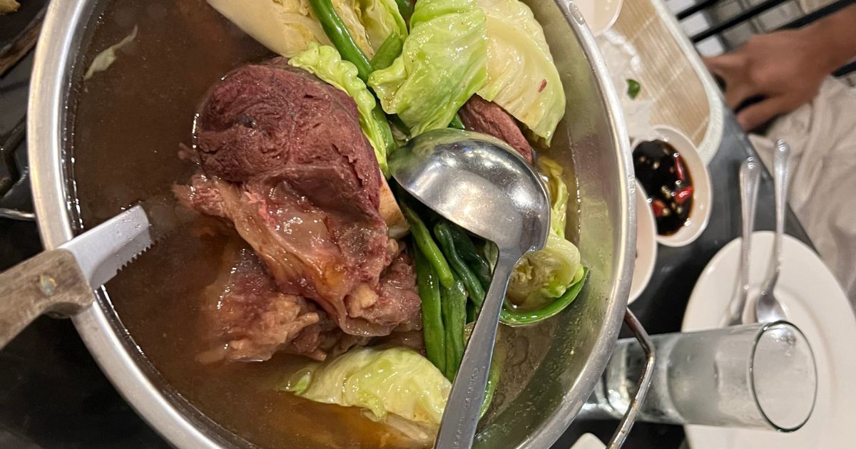 A pot of bulalo gently simmering on the stove with beef shanks and onion visible under a clear broth