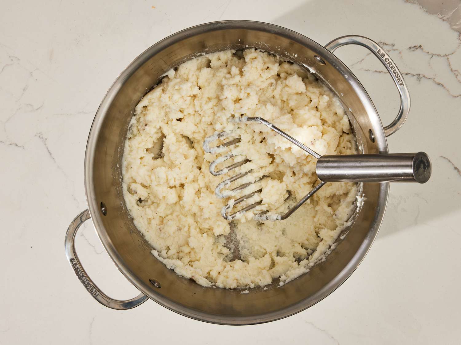 A pot of freshly mashed potatoes being stirred with butter, with steam rising in a warm home kitchen