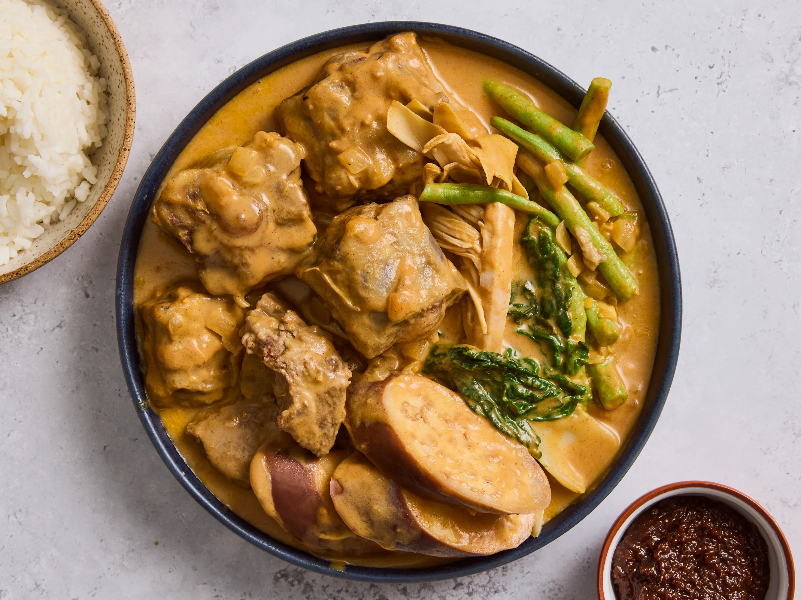 A pot of kare kare peanut sauce simmering on the stove with a wooden spoon resting on the rim