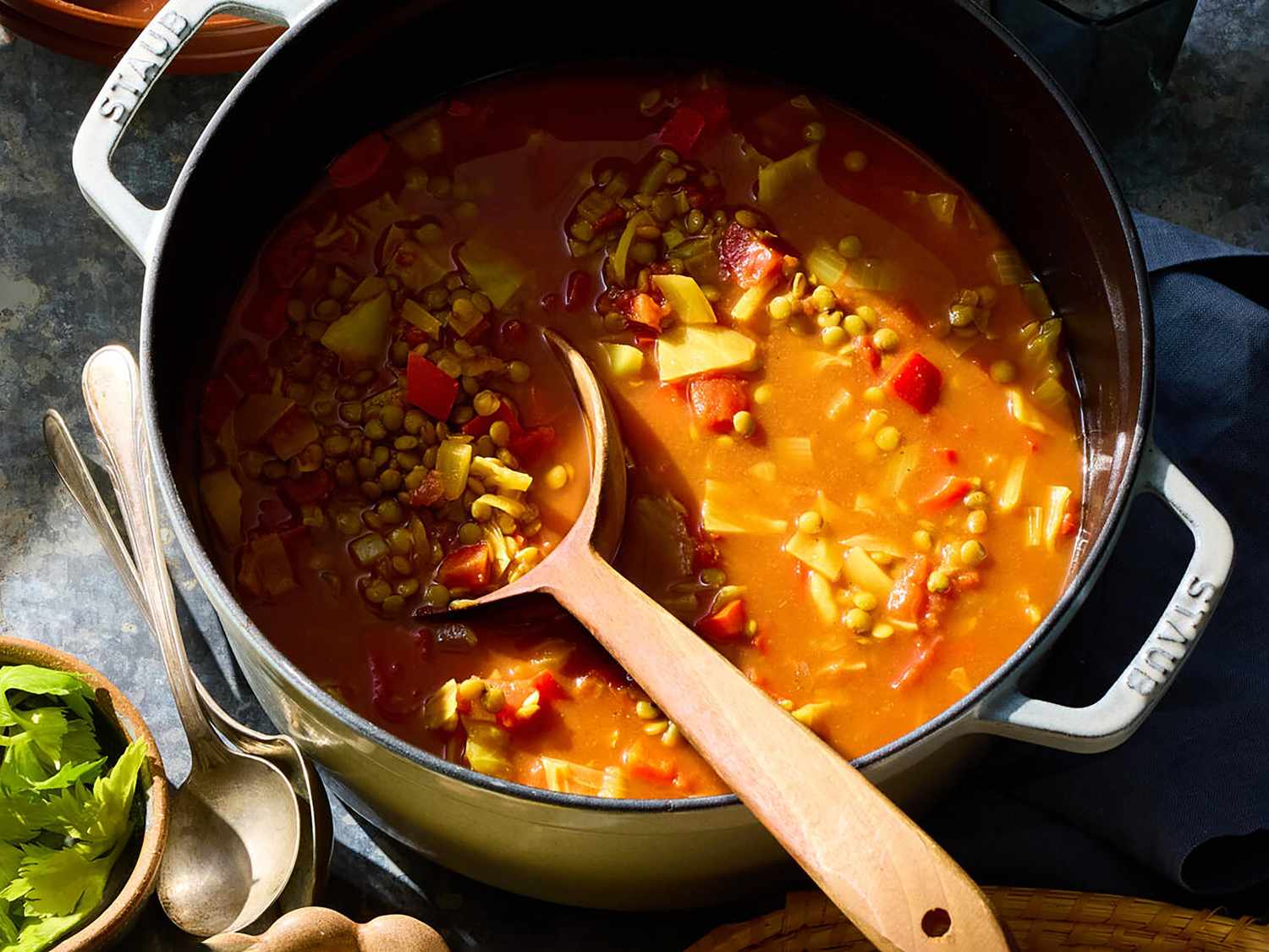 A pot of lentil and sweet potato stew gently simmering on a stovetop with a wooden spoon resting on the rim