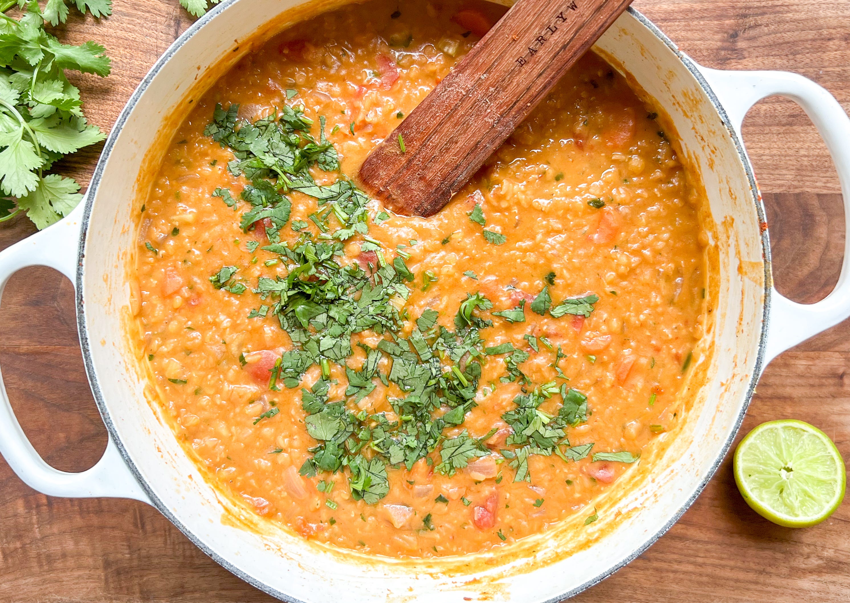 A pot of red lentil curry simmering on the stove with visible lentils and swirls of coconut milk, steam rising under warm kitchen lighting