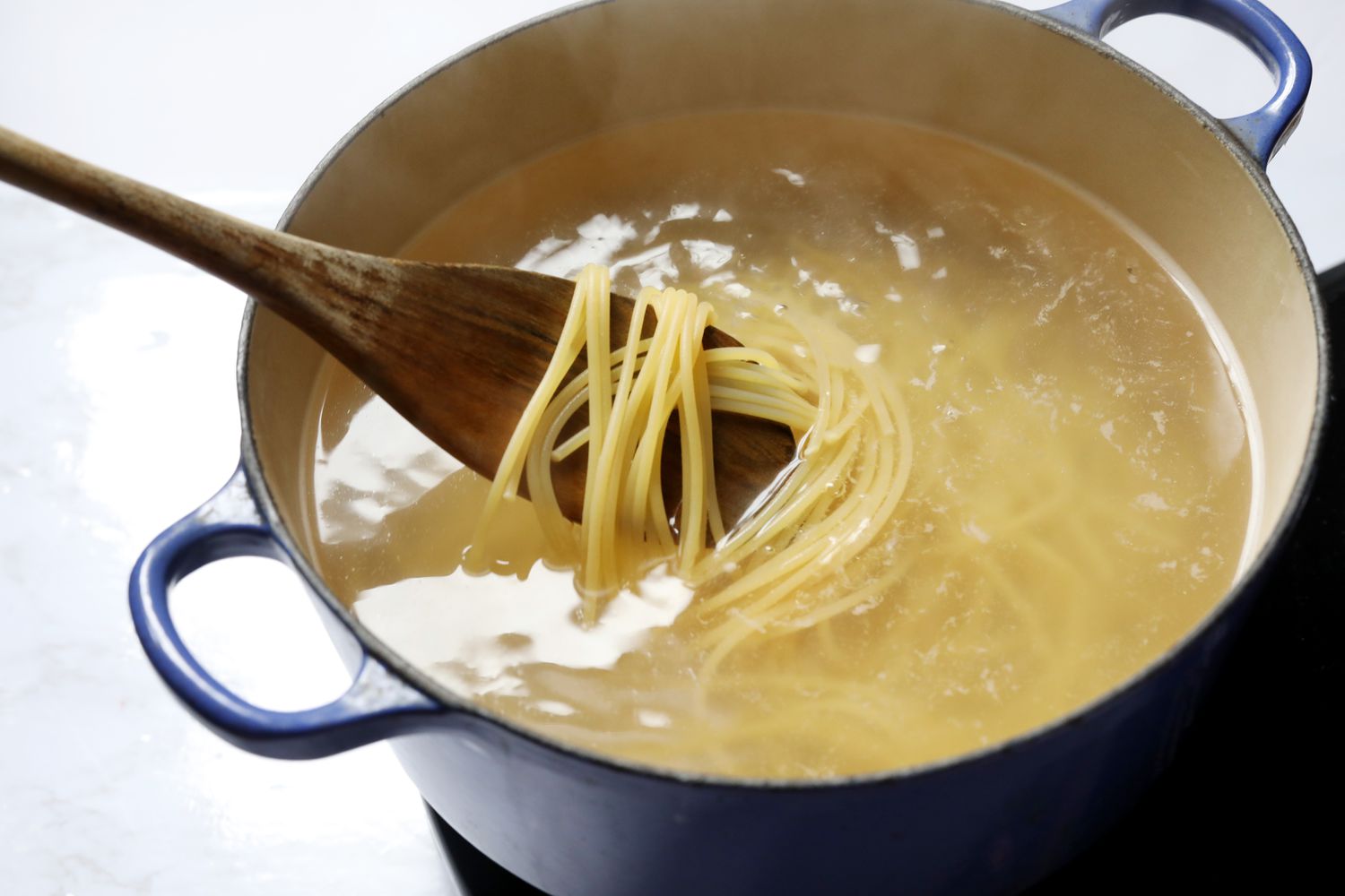 A pot of spaghetti boiling in salted water on a stove with steam rising