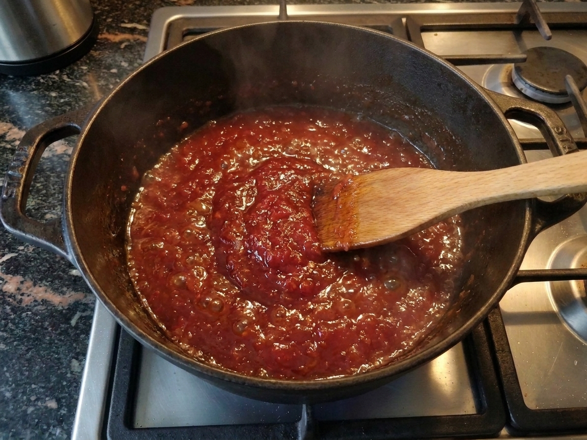 A pot of tomato mixture simmering and thickening into a glossy jam, with small bubbles breaking the surface