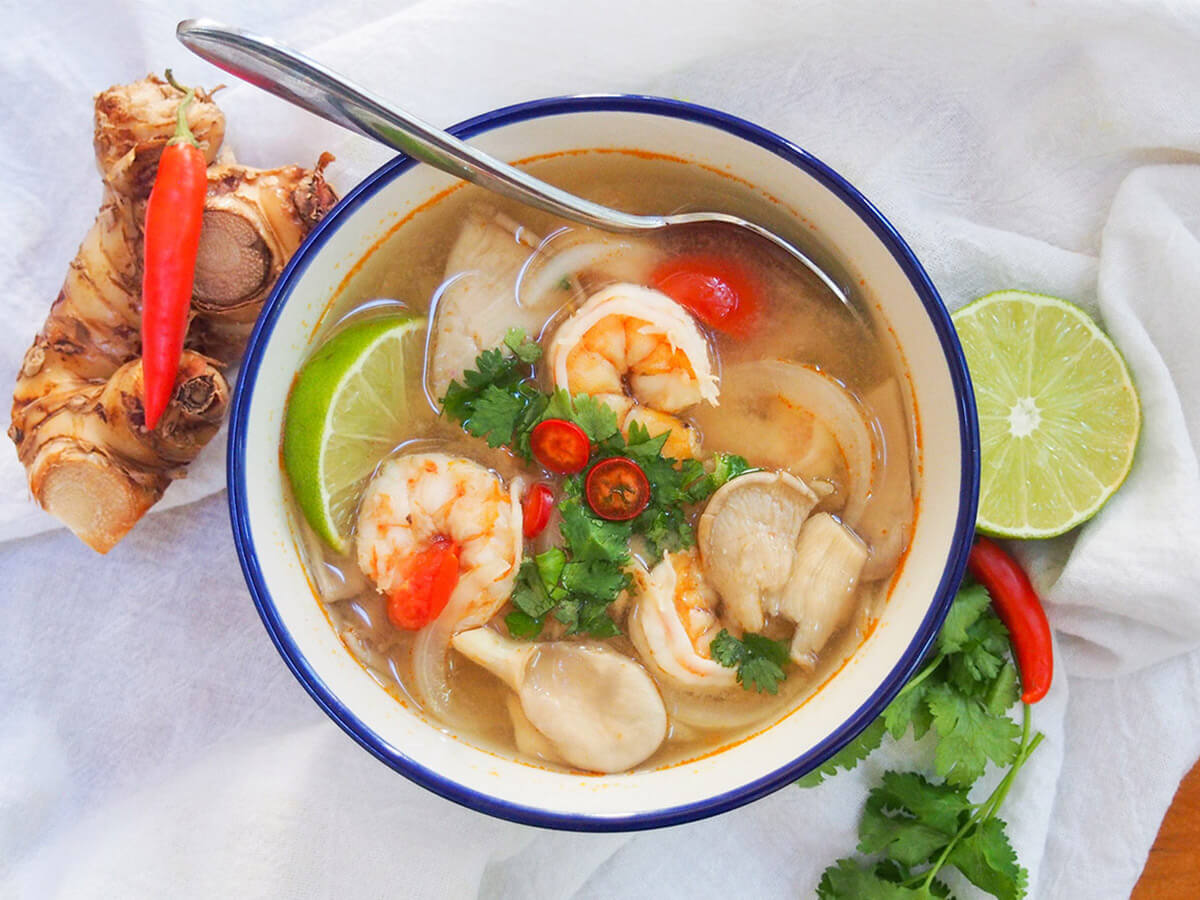 A pot on the stove with broth simmering and visible lemongrass pieces and makrut lime leaves floating on the surface