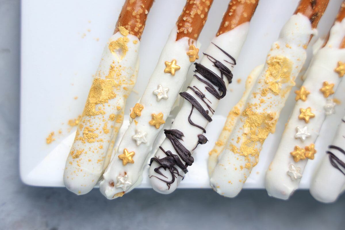 A pretzel rod being dipped into a bowl of melted white chocolate on a kitchen counter