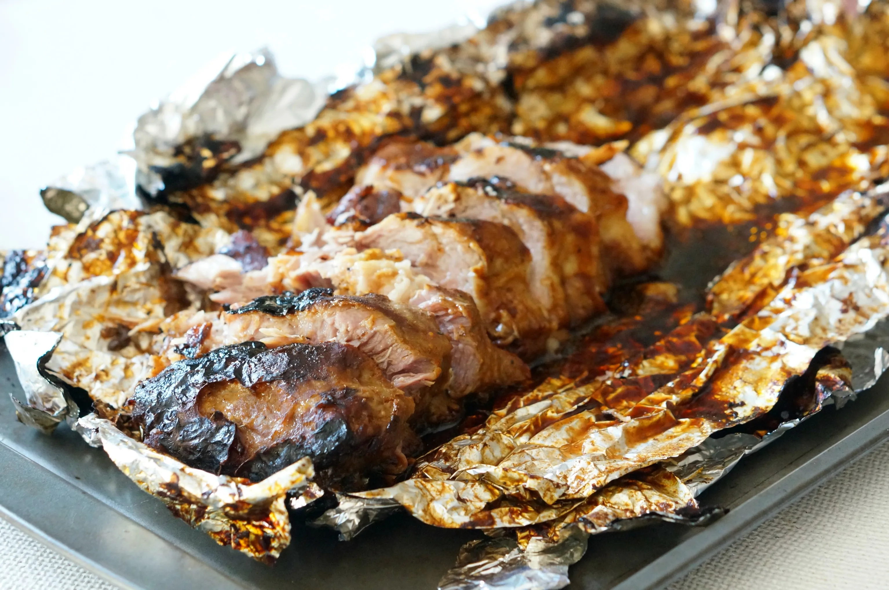 A rack of seasoned pork ribs tightly wrapped in aluminum foil on a rimmed sheet pan before going into the oven