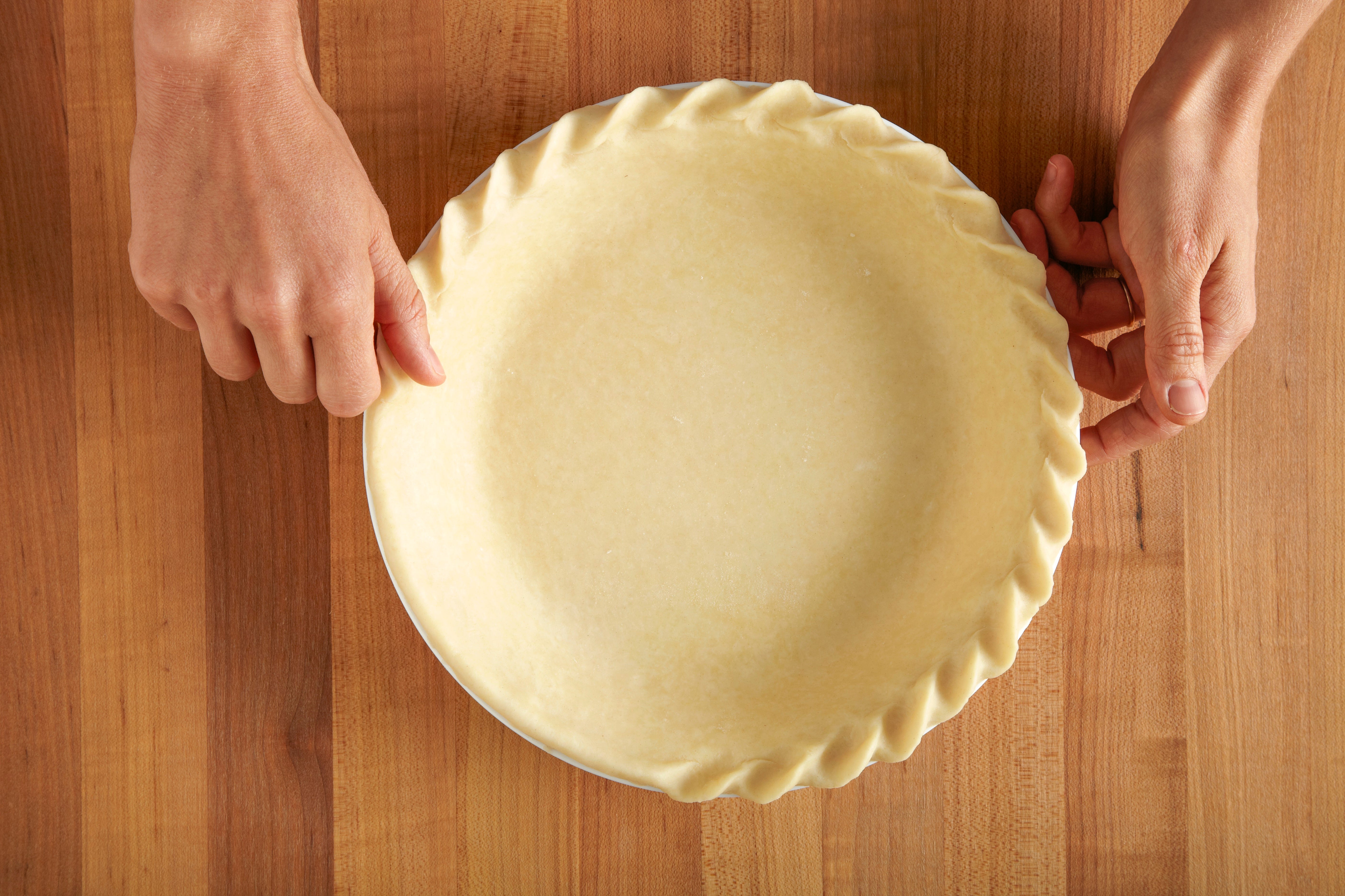 A raw pie crust fitted into a ceramic pie dish with a neat crimped edge, resting on a light kitchen counter