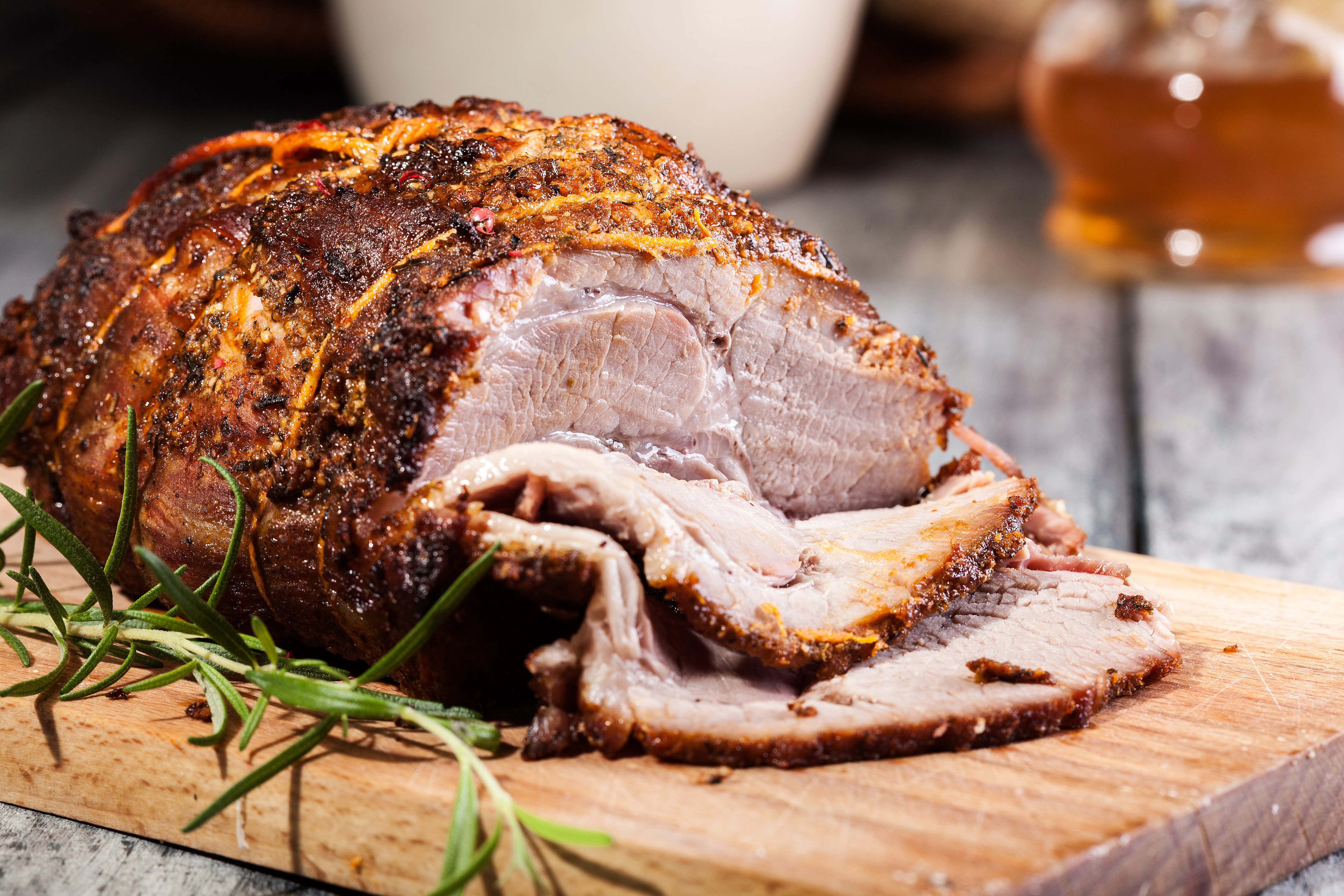 A raw pork butt roast on a cutting board with bowls of brown sugar, paprika, salt, pepper, garlic powder, sliced onion, and bottles of apple cider vinegar and Worcestershire on a kitchen counter