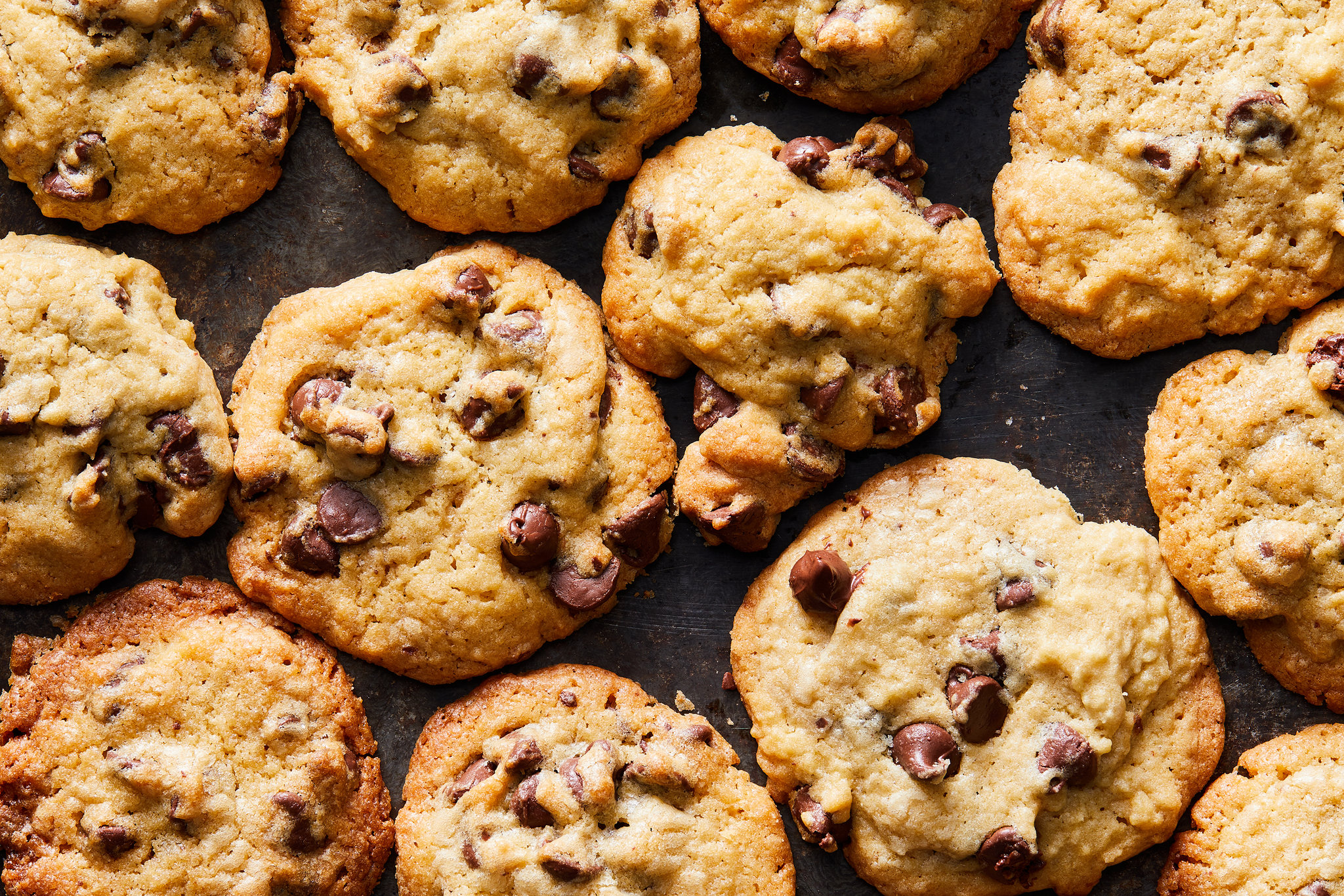 A real photo of classic chocolate chip cookies with crisp edges and chewy centers cooling on a wire rack on a warm-toned kitchen counter
