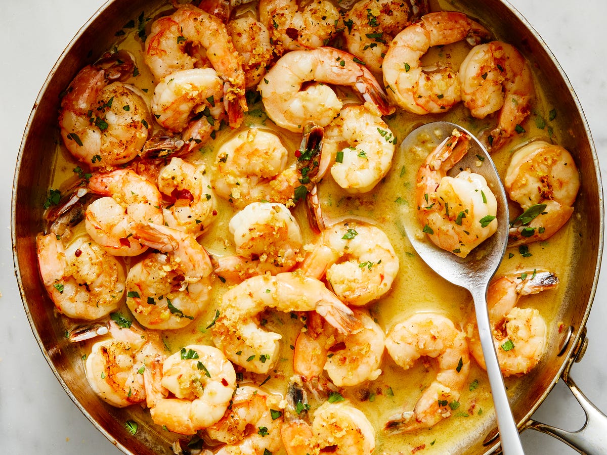 A real photograph close up of shrimp coated in a glossy garlic butter lemon sauce with black pepper and parsley