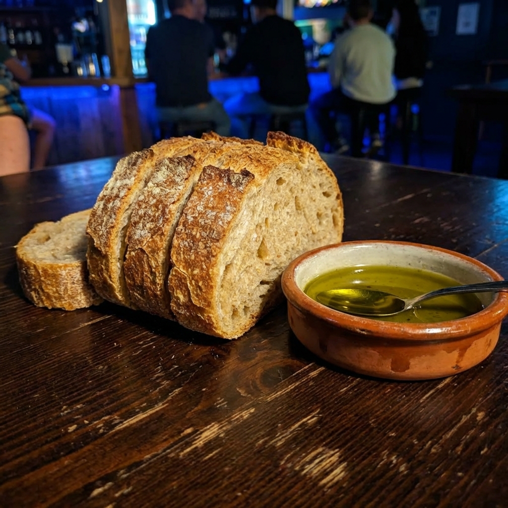 A real photograph of rustic bread slices and a small dish of olive oil on a table