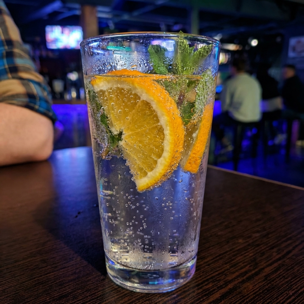 A real photograph of sparkling water with orange slices and mint in a tall glass with condensation