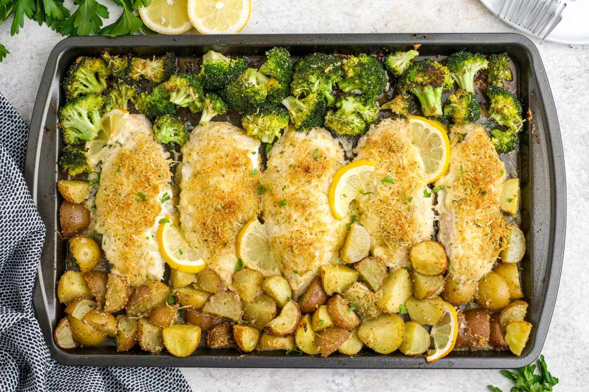 A rimmed baking sheet filled with roasted lemon garlic chicken thighs, golden baby potatoes, and charred broccoli florets on a warm kitchen counter