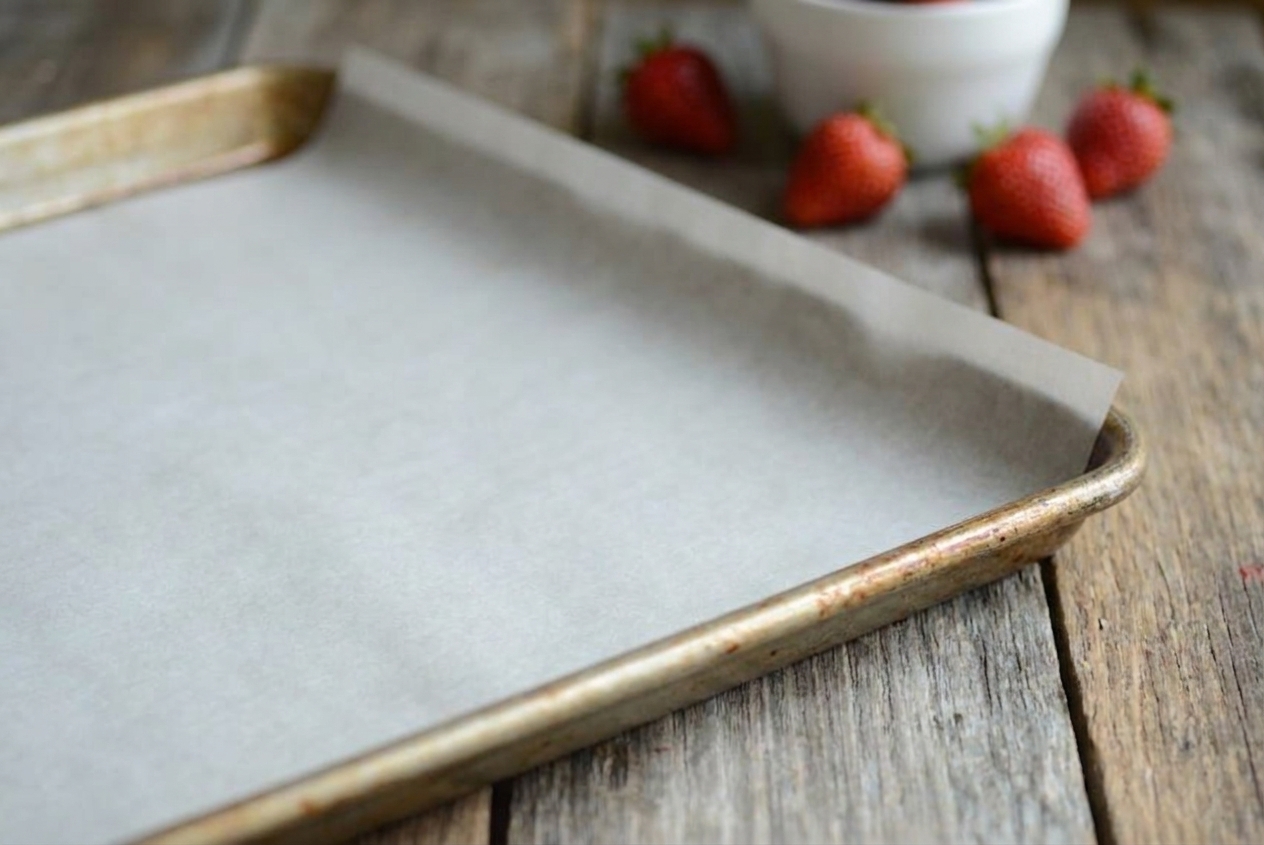 A rimmed baking sheet lined with parchment paper on a clean kitchen counter, edges smoothed flat