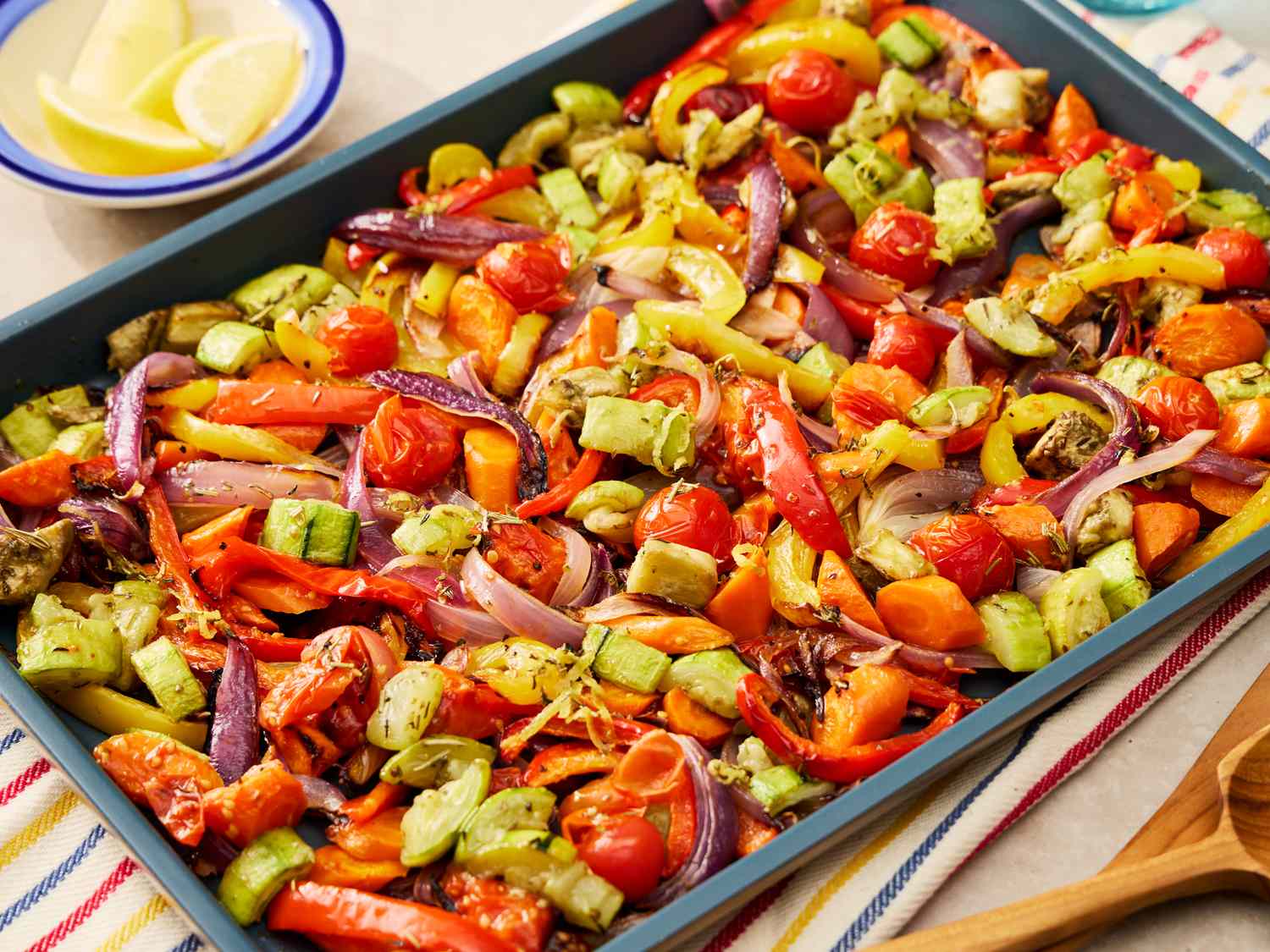 A rimmed baking sheet of vegetables roasting in an oven with lightly browned edges