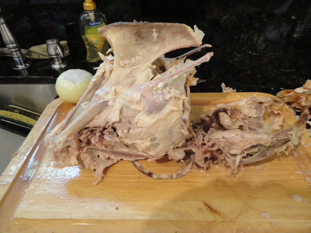 A roasted turkey carcass on a cutting board with picked clean bones and a small pile of skin and scraps nearby on a kitchen counter