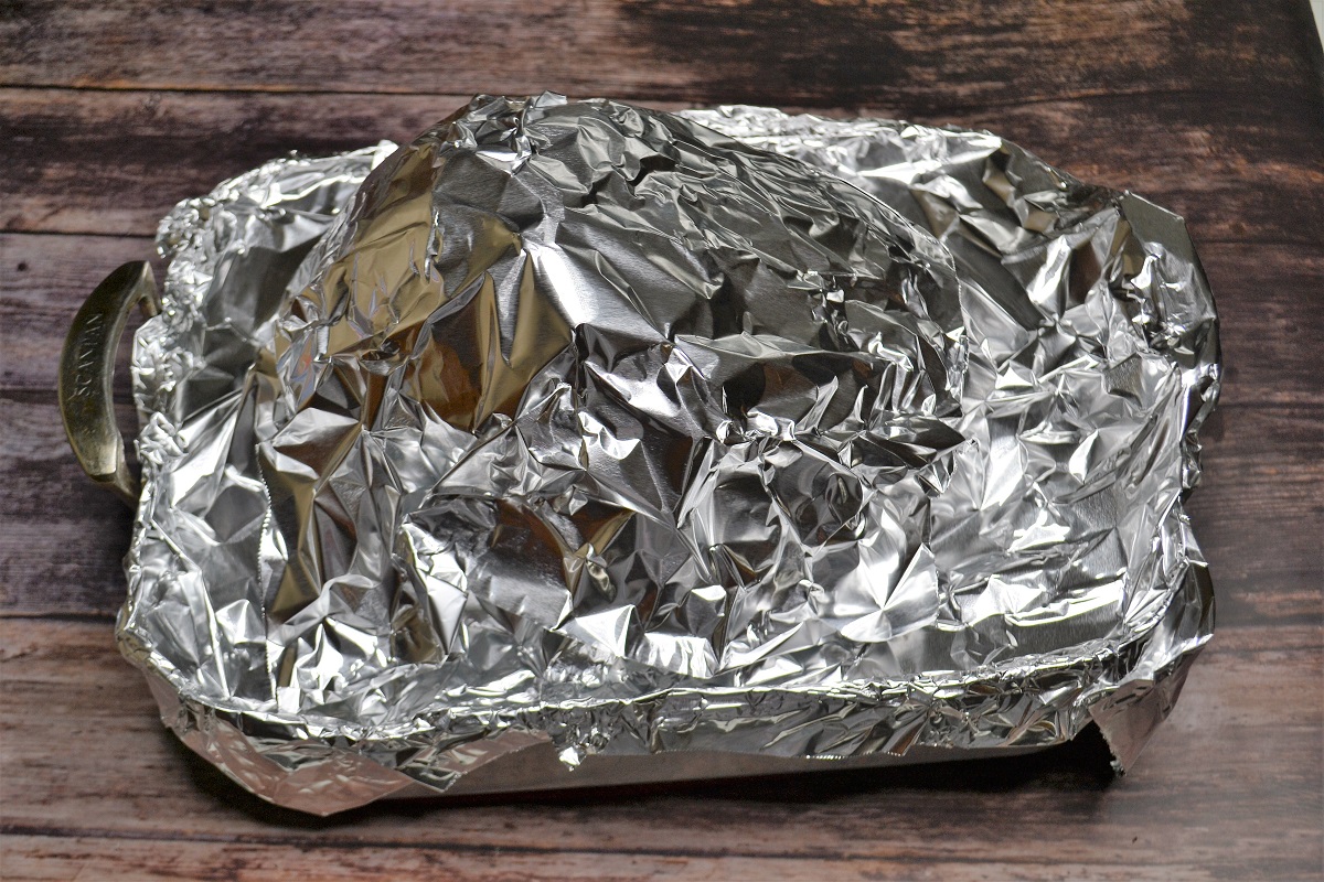 A roasting pan with a spiral-sliced ham tightly covered in aluminum foil on a kitchen counter, ready for the oven