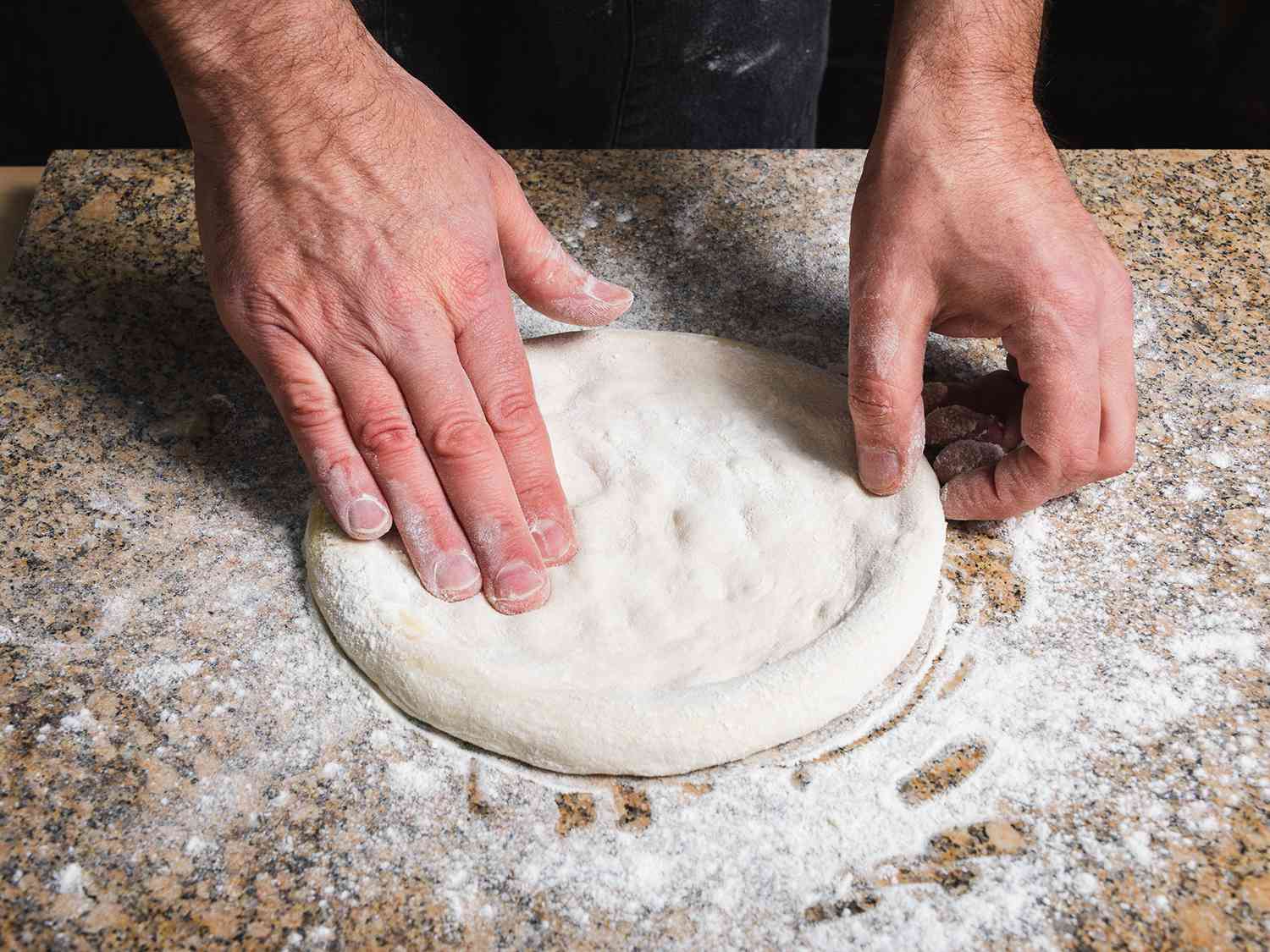 A round of homemade pizza dough stretched into a thin circle on a floured wooden countertop, with a rim left slightly thicker for the crust