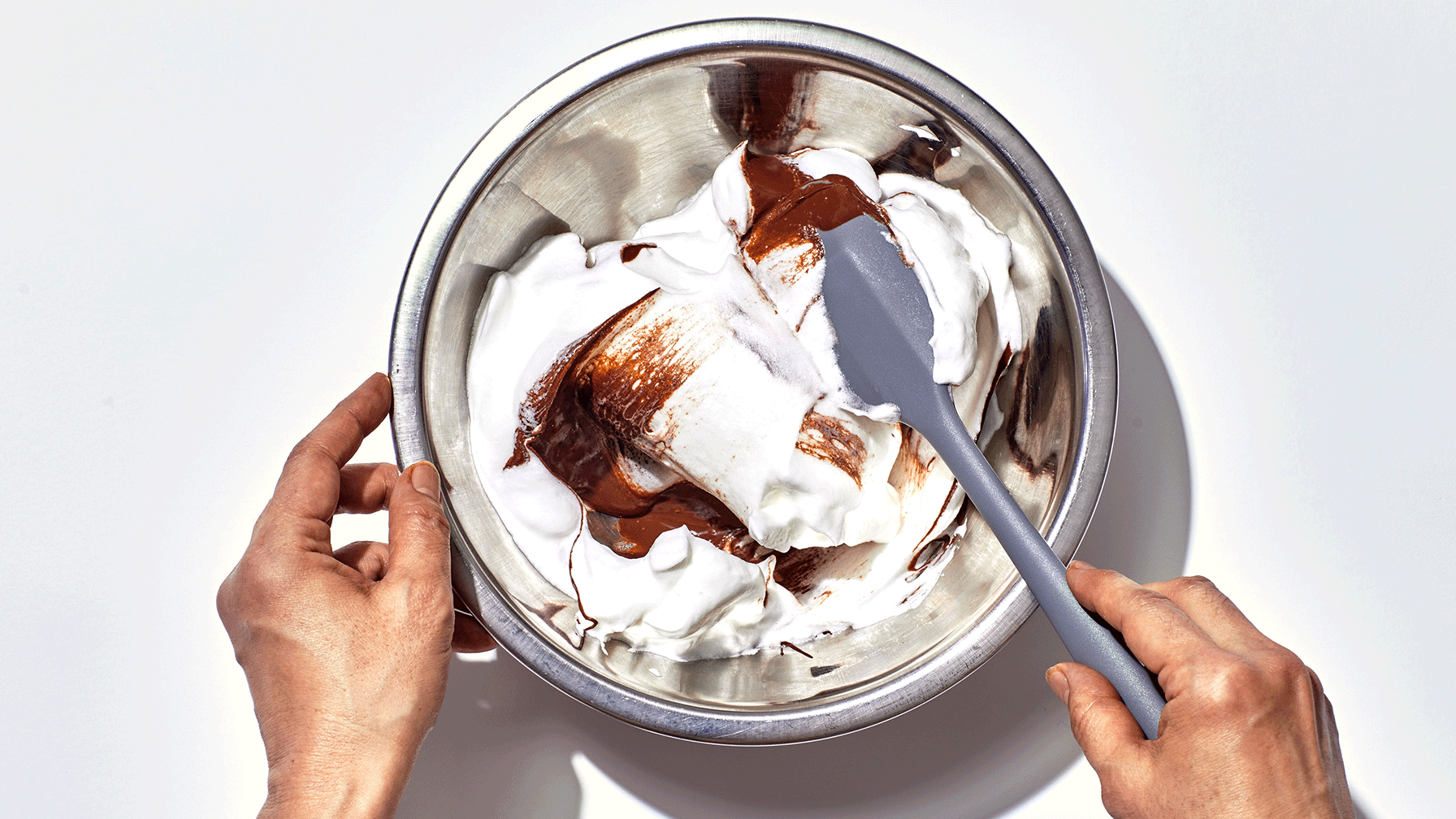 A rubber spatula folding whipped topping into thick vanilla pudding in a large bowl on a kitchen counter