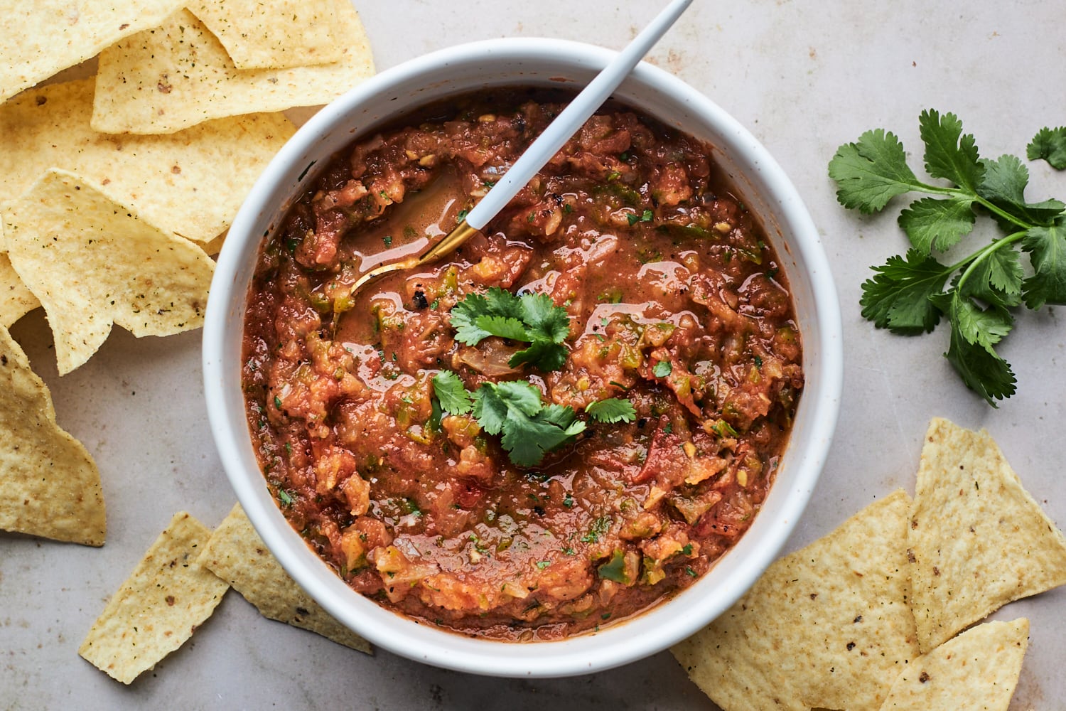 A rustic bowl of deep red salsa roja on a wooden table with tortilla chips nearby, warm kitchen lighting