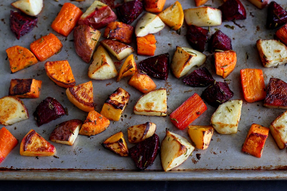 A rustic sheet pan of roasted root vegetables with browned edges and fresh herbs on top, set on a kitchen counter